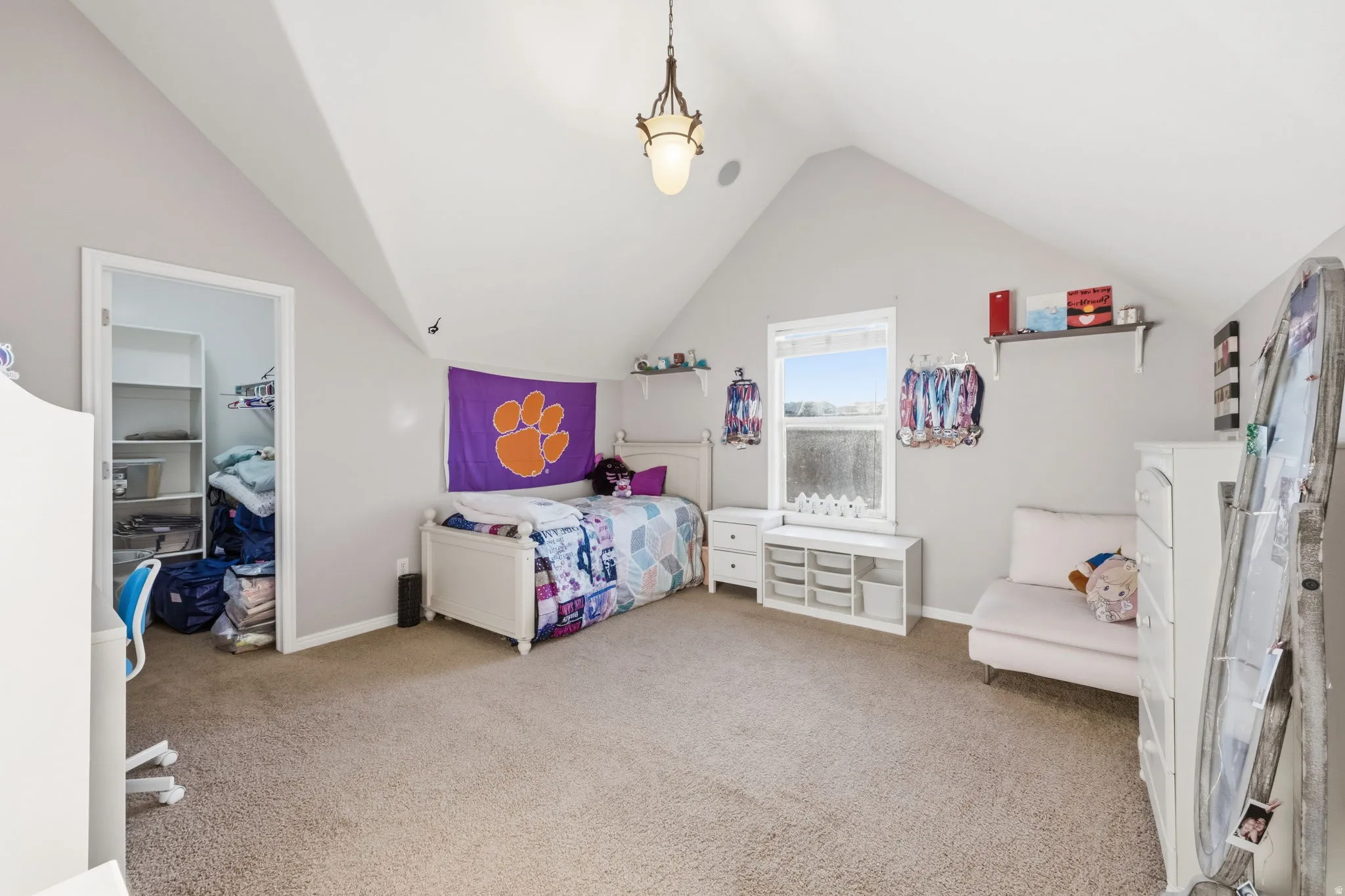 Spacious room featuring vaulted ceilings, a window with a built-in storage bench, soft carpeting, a built-in ceiling speaker, and an overhead light fixture