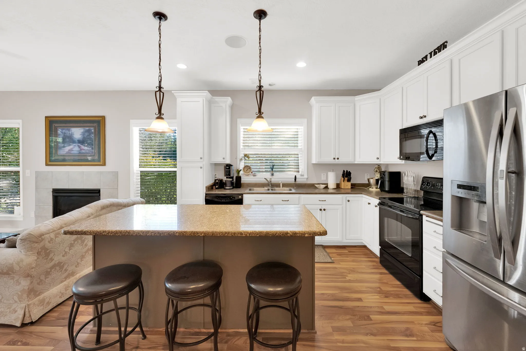 Open-concept kitchen featuring white cabinetry, stone-finish countertops, stainless steel refrigerator, and wood-finish flooring