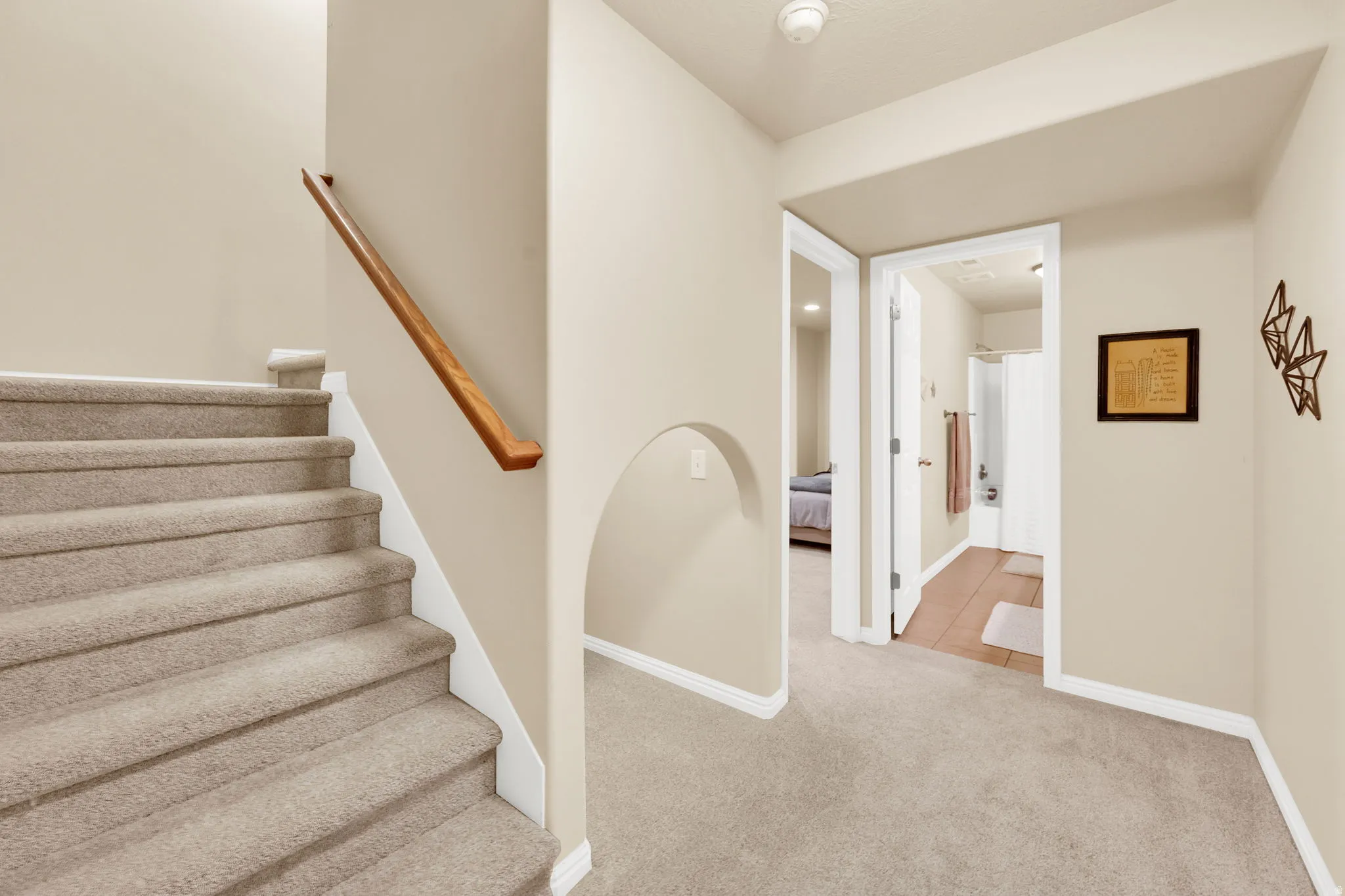 Carpeted staircase with a wood handrail, featuring an arched hallway entry, neutral wall tones, and white trim