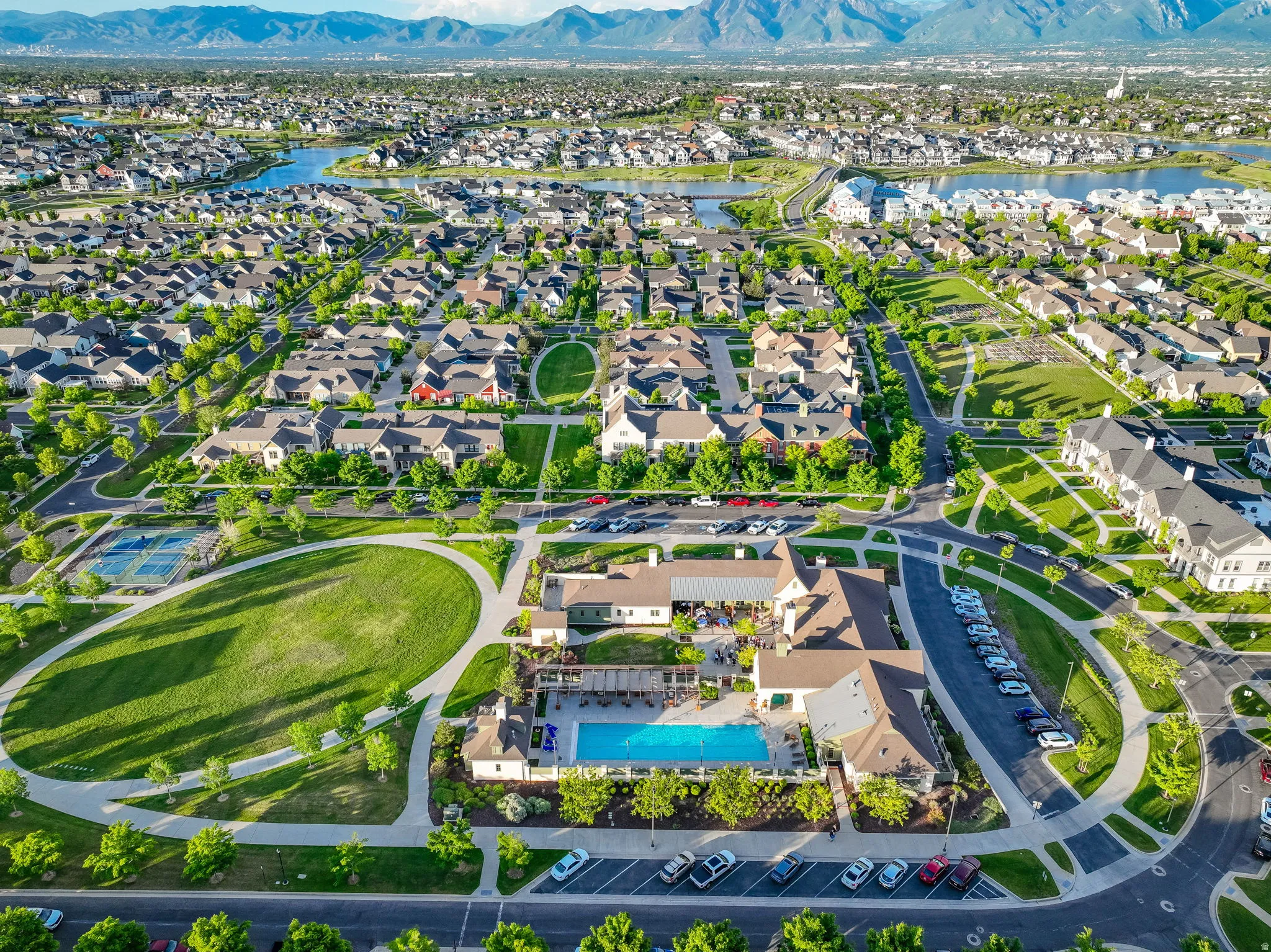 Expansive community amenities including a swimming pool with lounge areas, a large central green space, and a tennis court