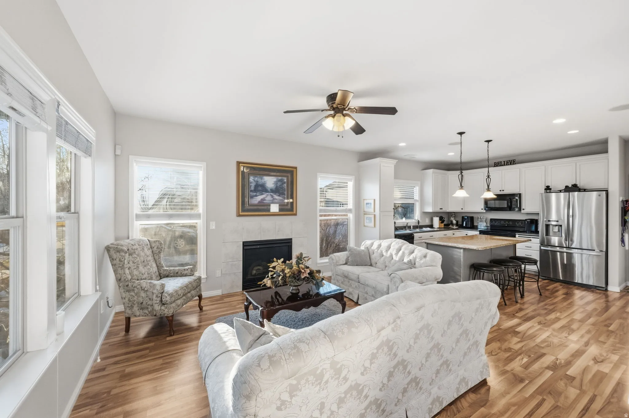 Open-concept living area featuring wood-finish flooring, a ceiling fan, and multiple windows