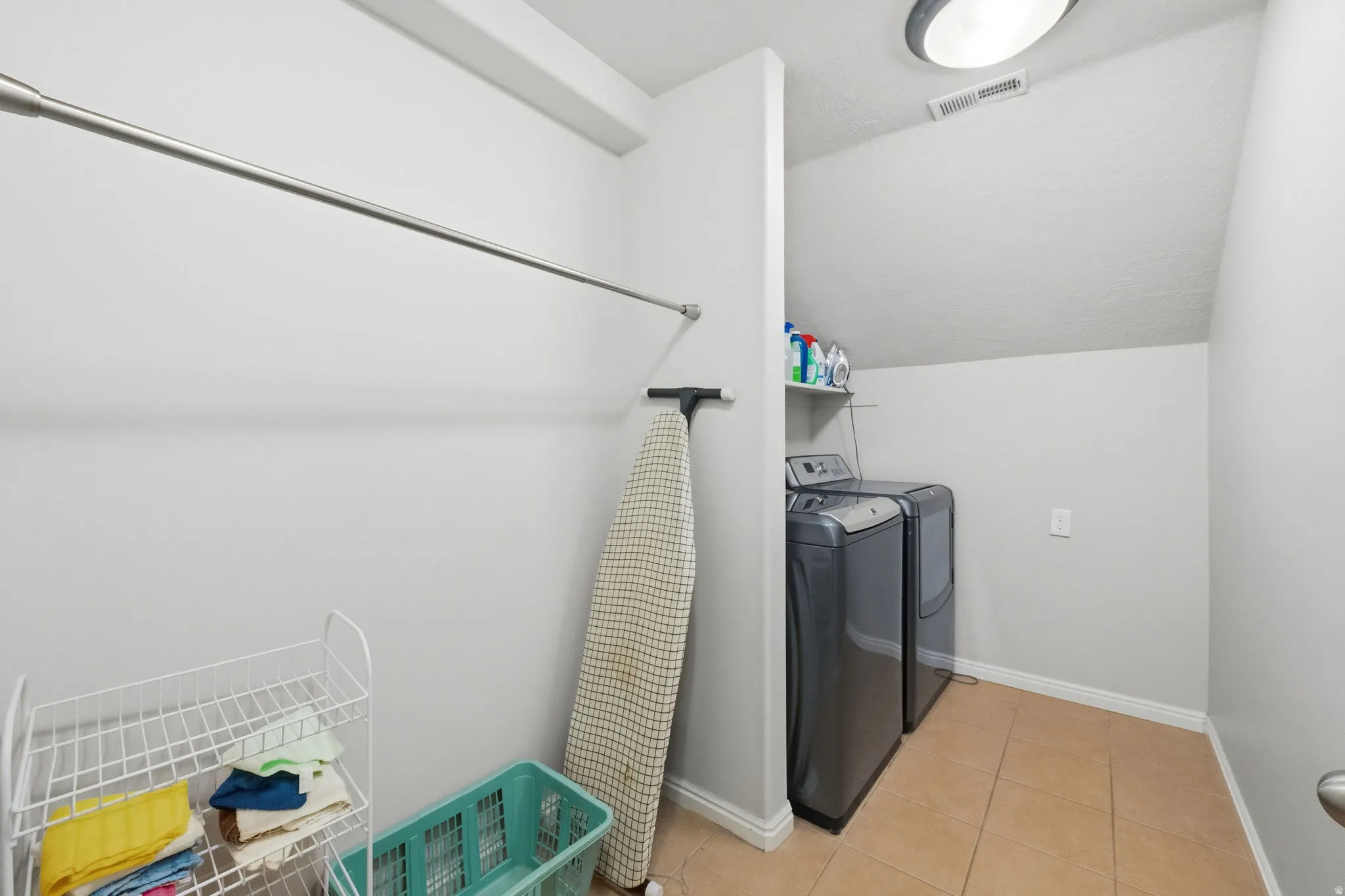 Dedicated laundry area featuring tile flooring, a wall-mounted shelving unit, and a clothing rod