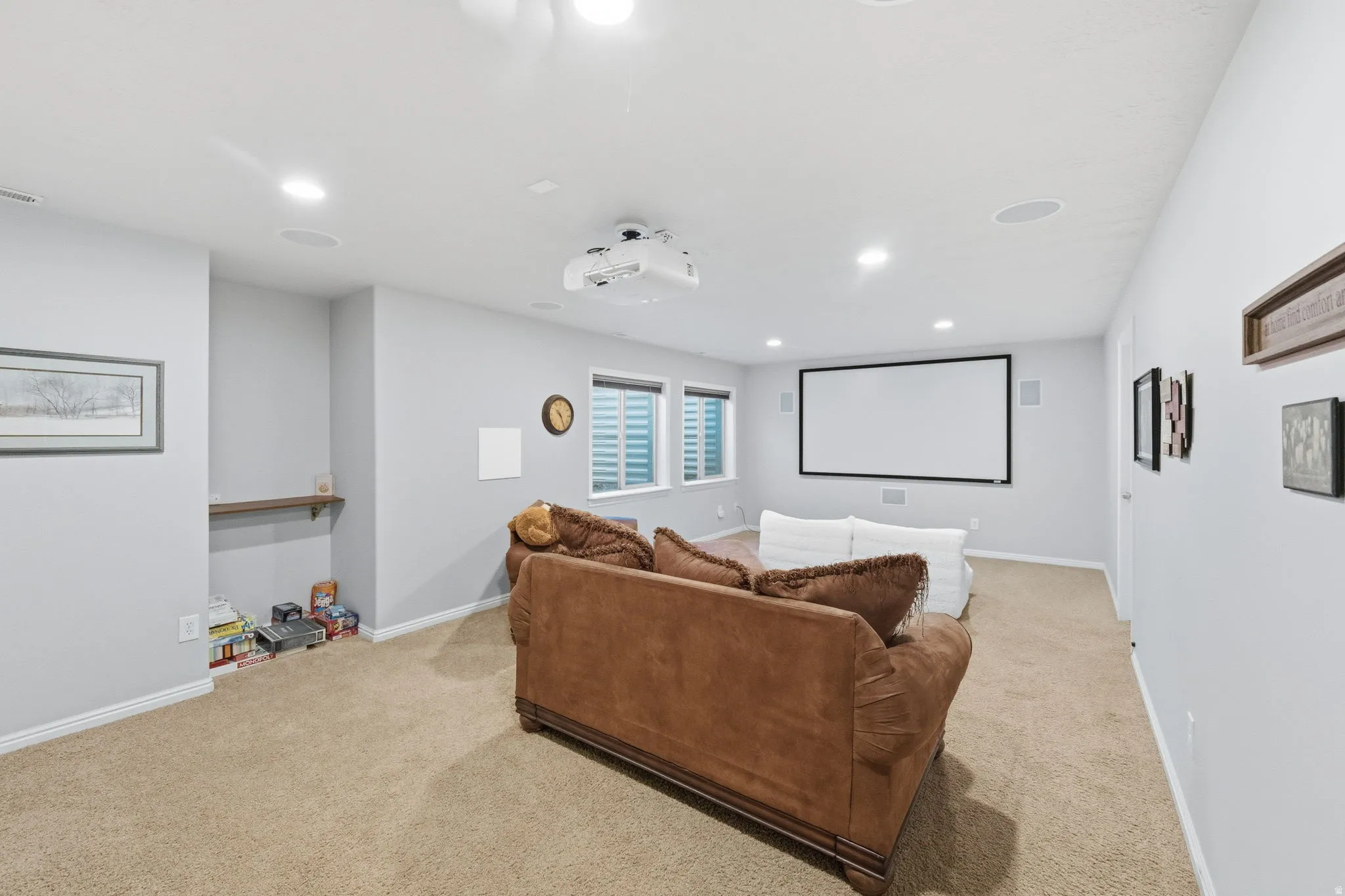 Spacious entertainment area featuring a ceiling-mounted projector, large projection screen, recessed lighting, and integrated ceiling speakers