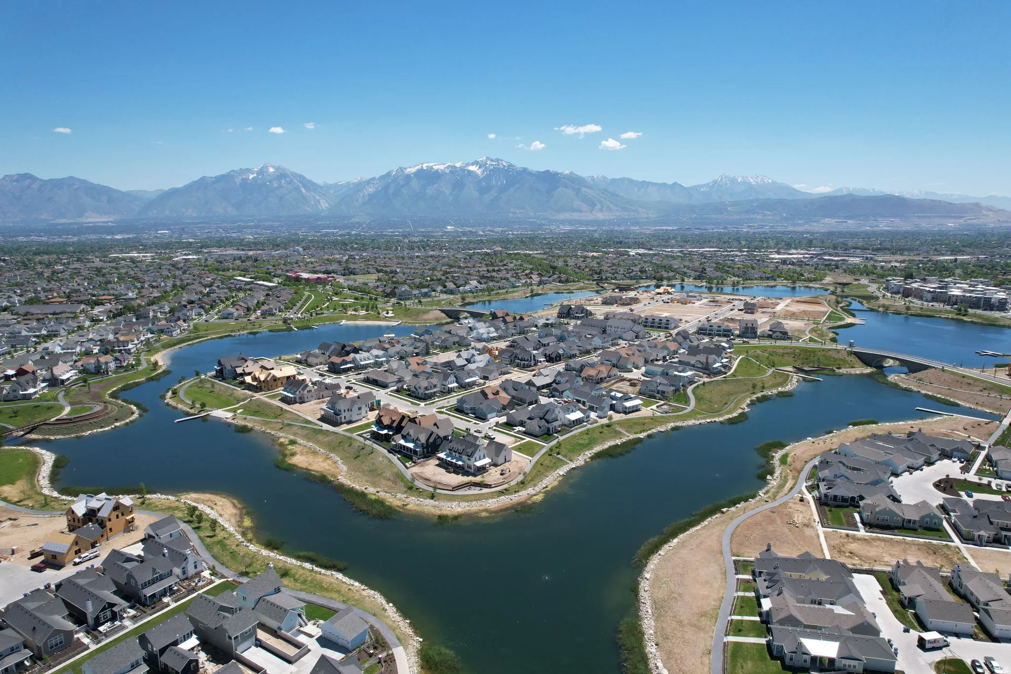 Expansive residential development featuring a large central lake with multiple inlets, surrounding homes, paved pathways, and distant snow-capped mountains