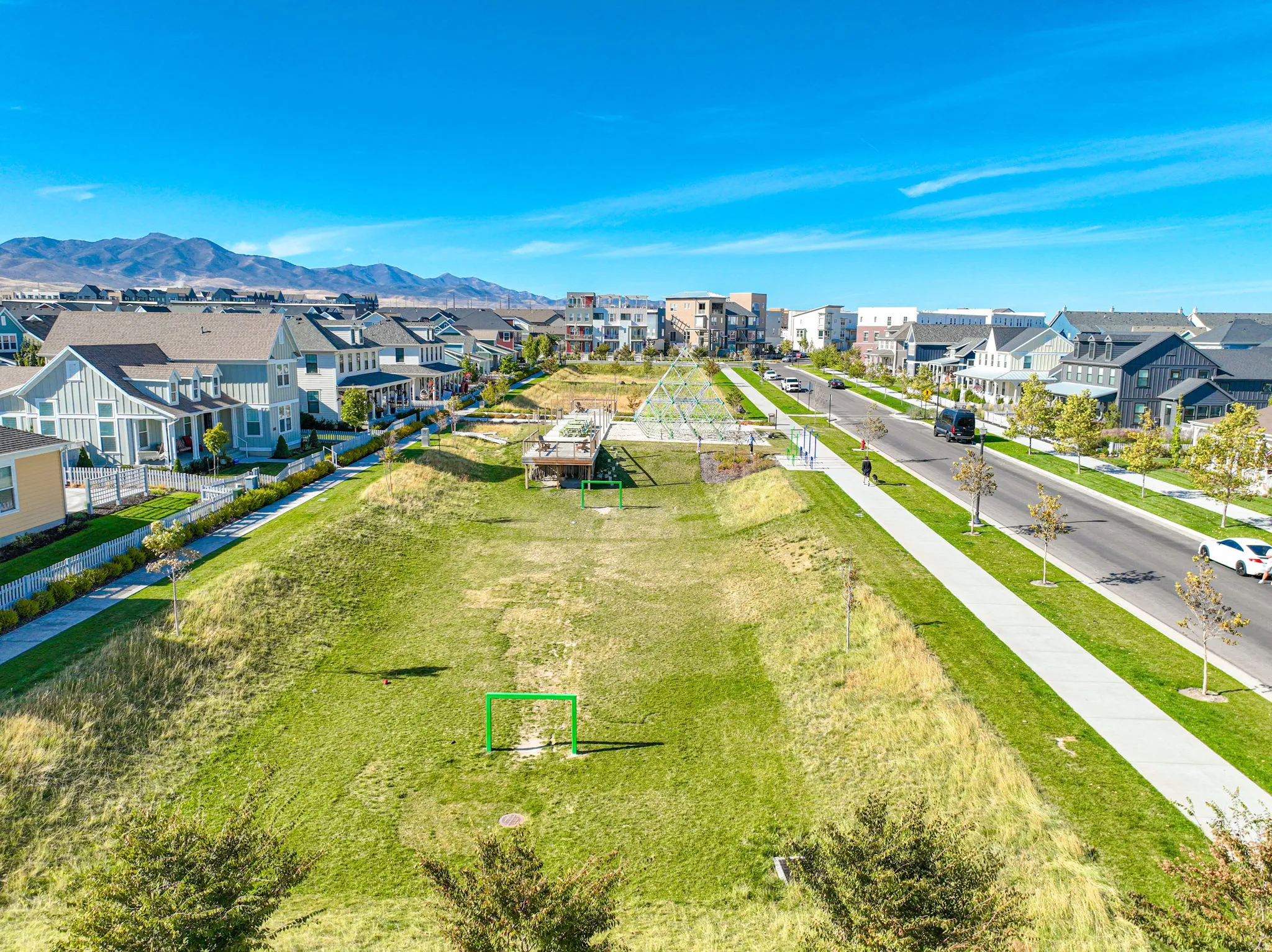 Expansive green space with a recreational goal, bordered by a pedestrian pathway and residential properties