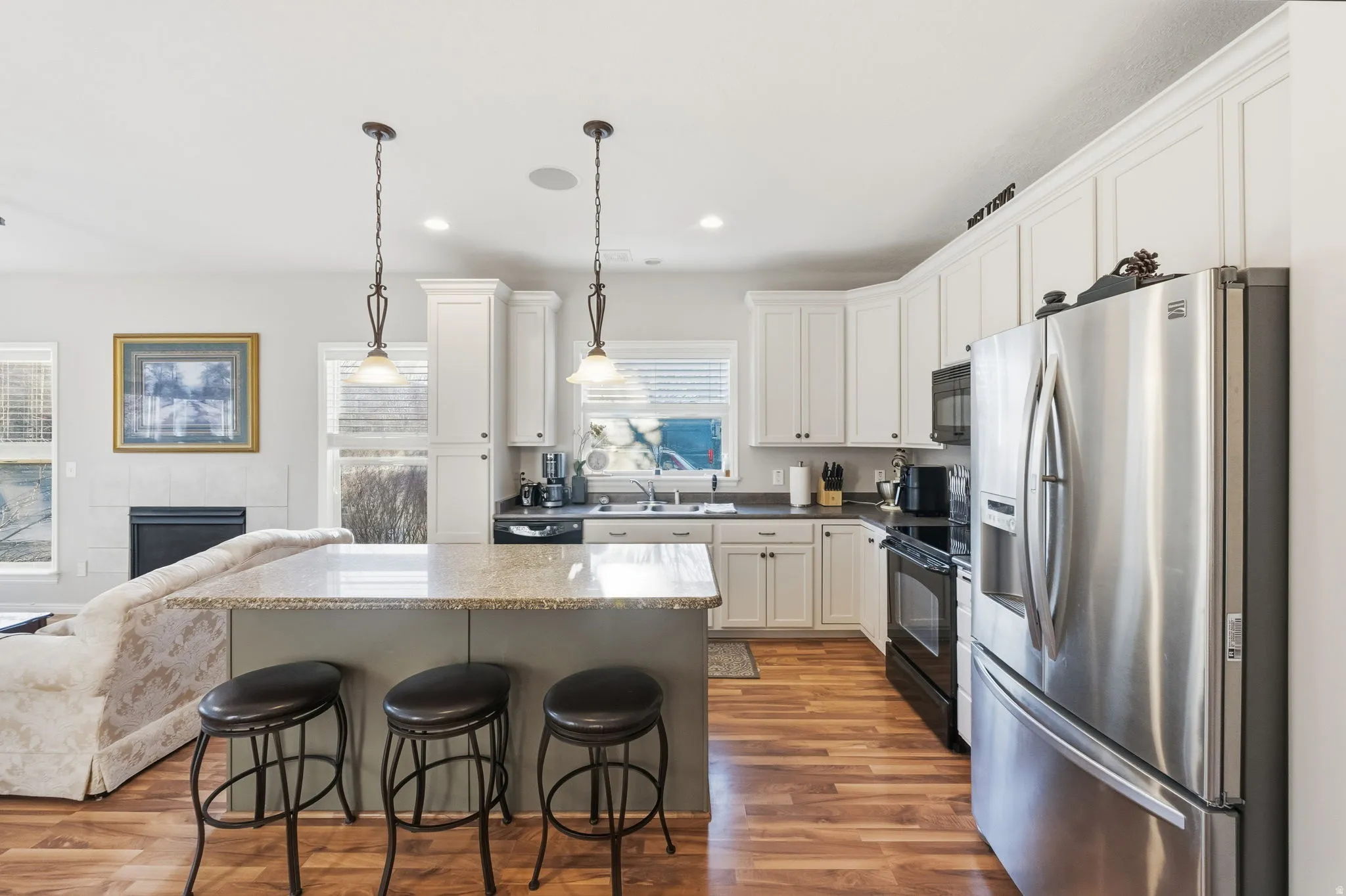 Open-concept kitchen featuring wood-finish flooring, white cabinetry, dark countertops, and a stainless steel refrigerator