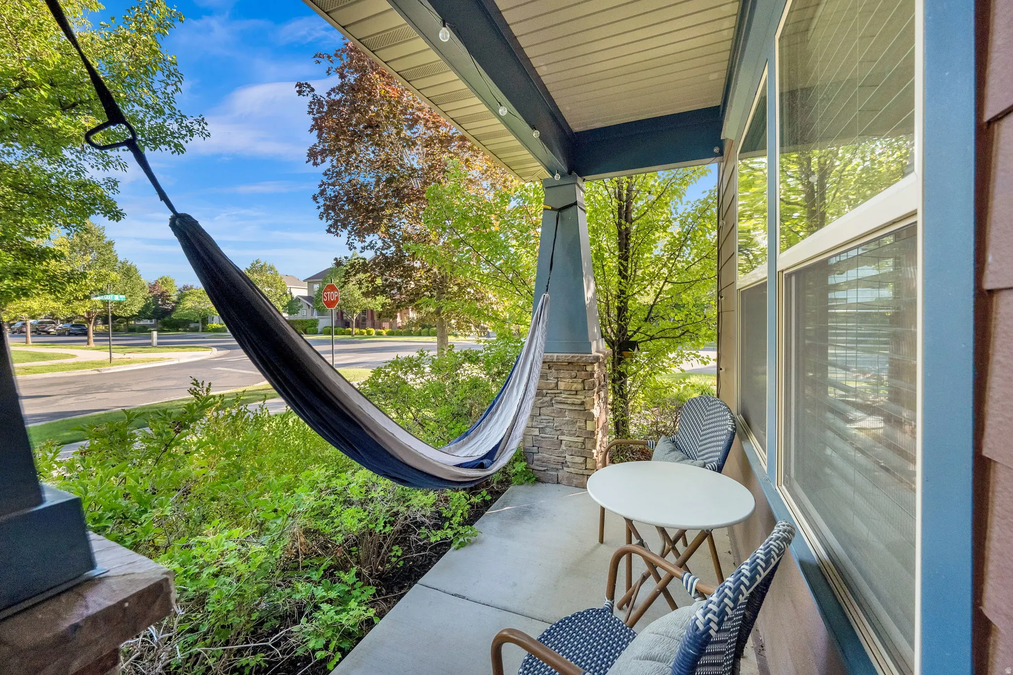 Covered front porch featuring a stacked stone pillar, concrete flooring, and windows with white blinds