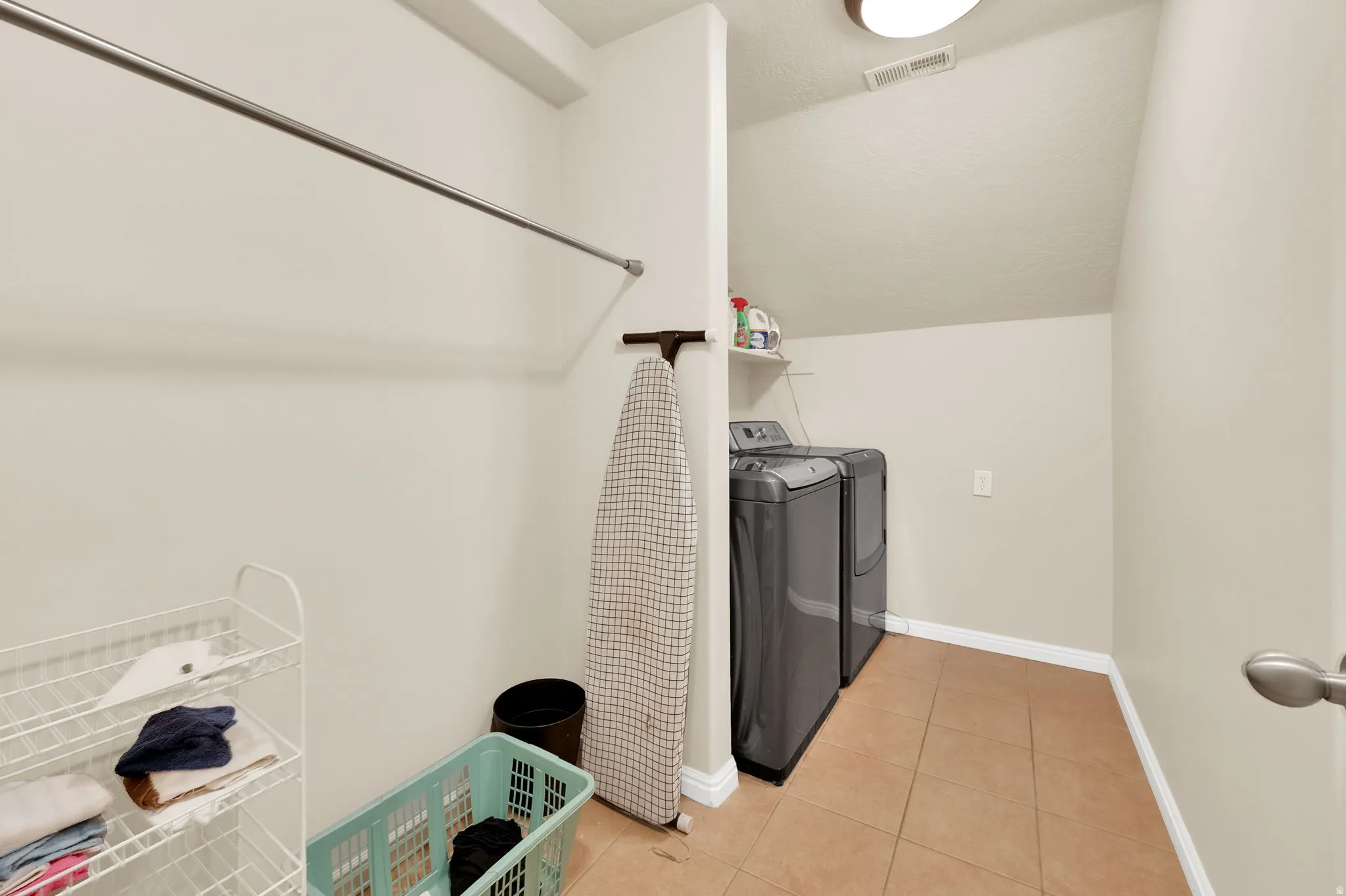 Dedicated laundry room featuring ceramic tile flooring, a built-in hanging rod, and sloped ceiling architecture