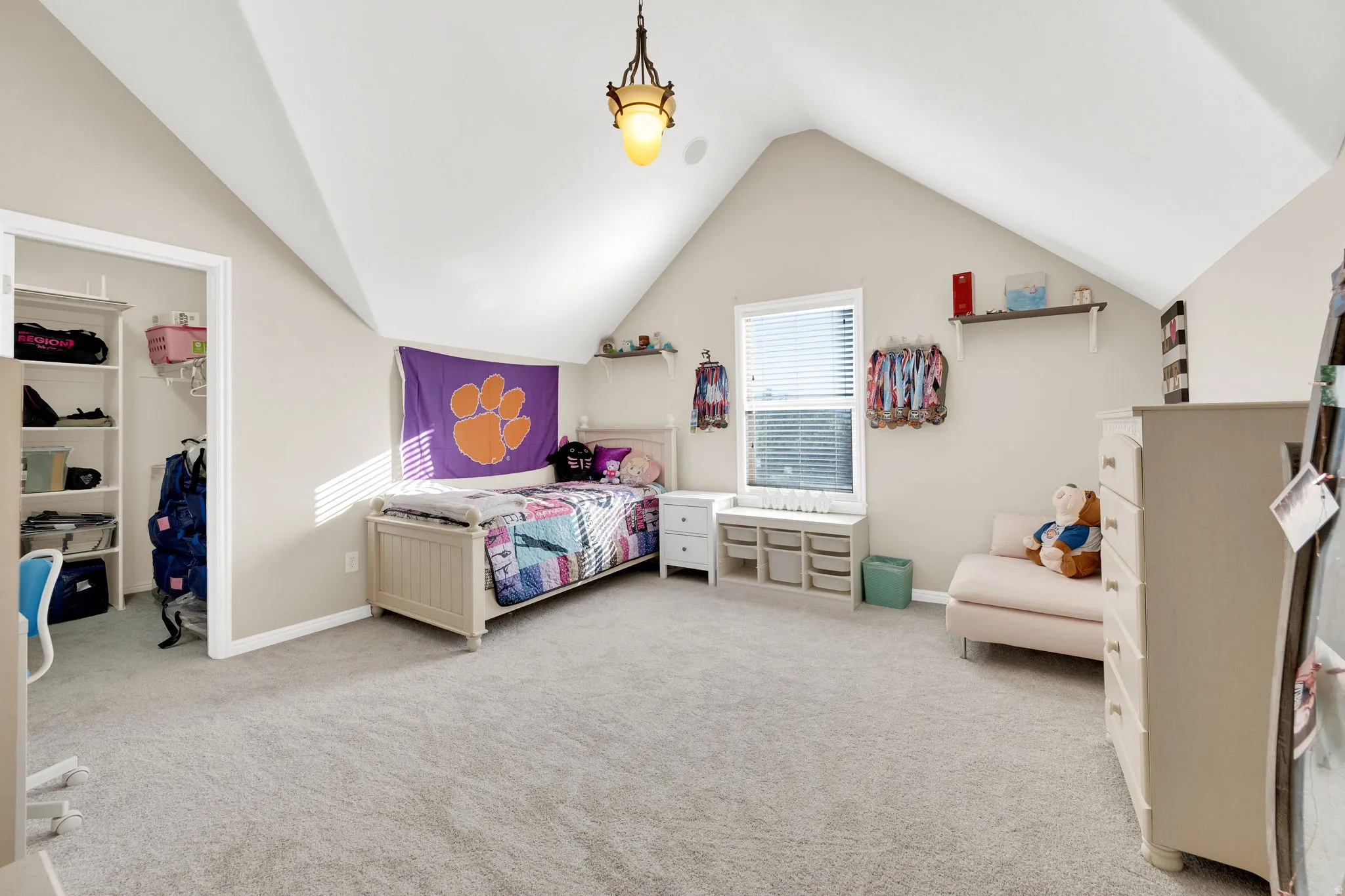 Room featuring sloped ceilings, light-colored carpeting, a single window with blinds, and a built-in closet with shelving