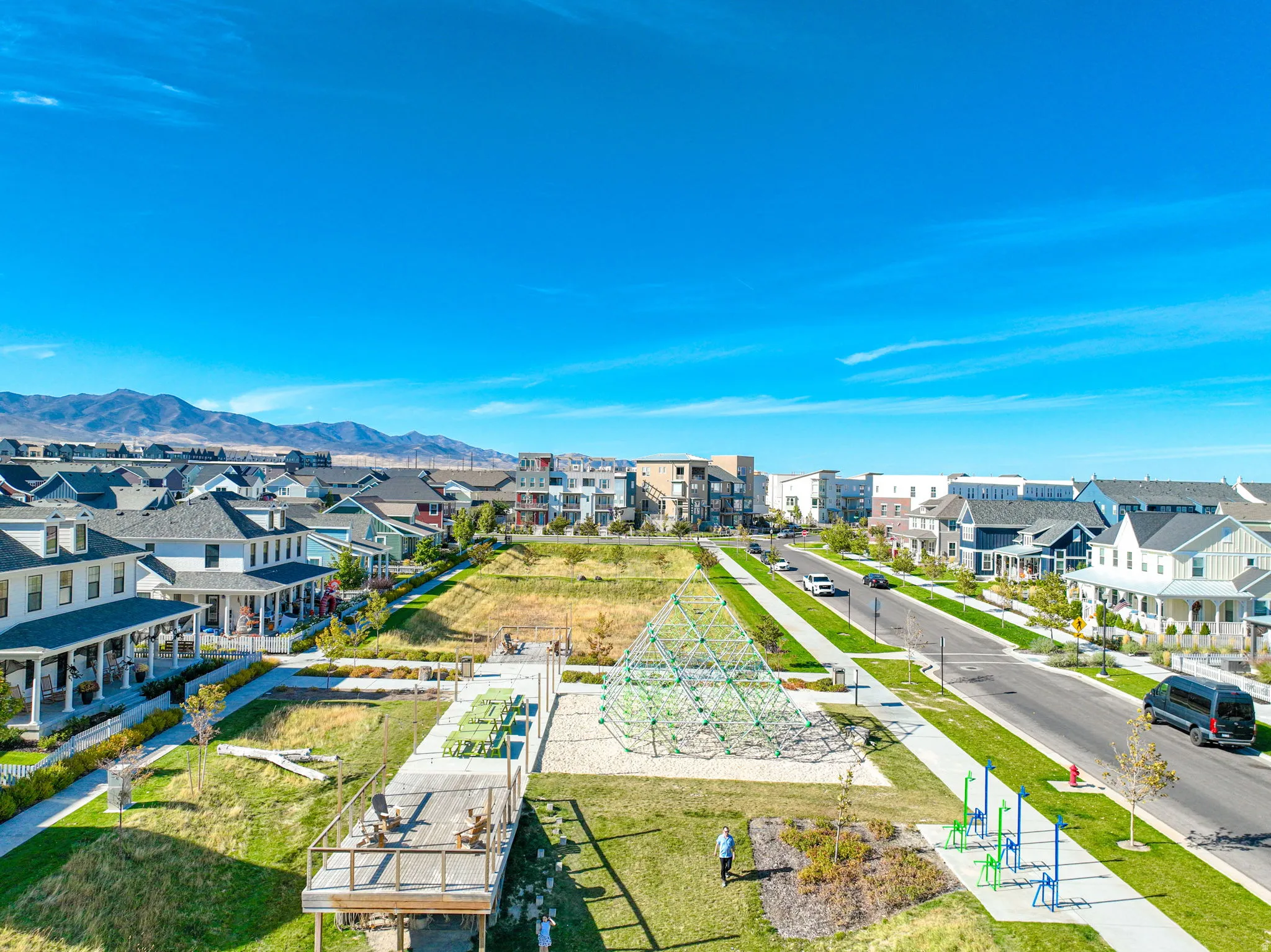 Expansive community green space featuring a geometric climbing structure, a wooden deck, and a modern fitness area