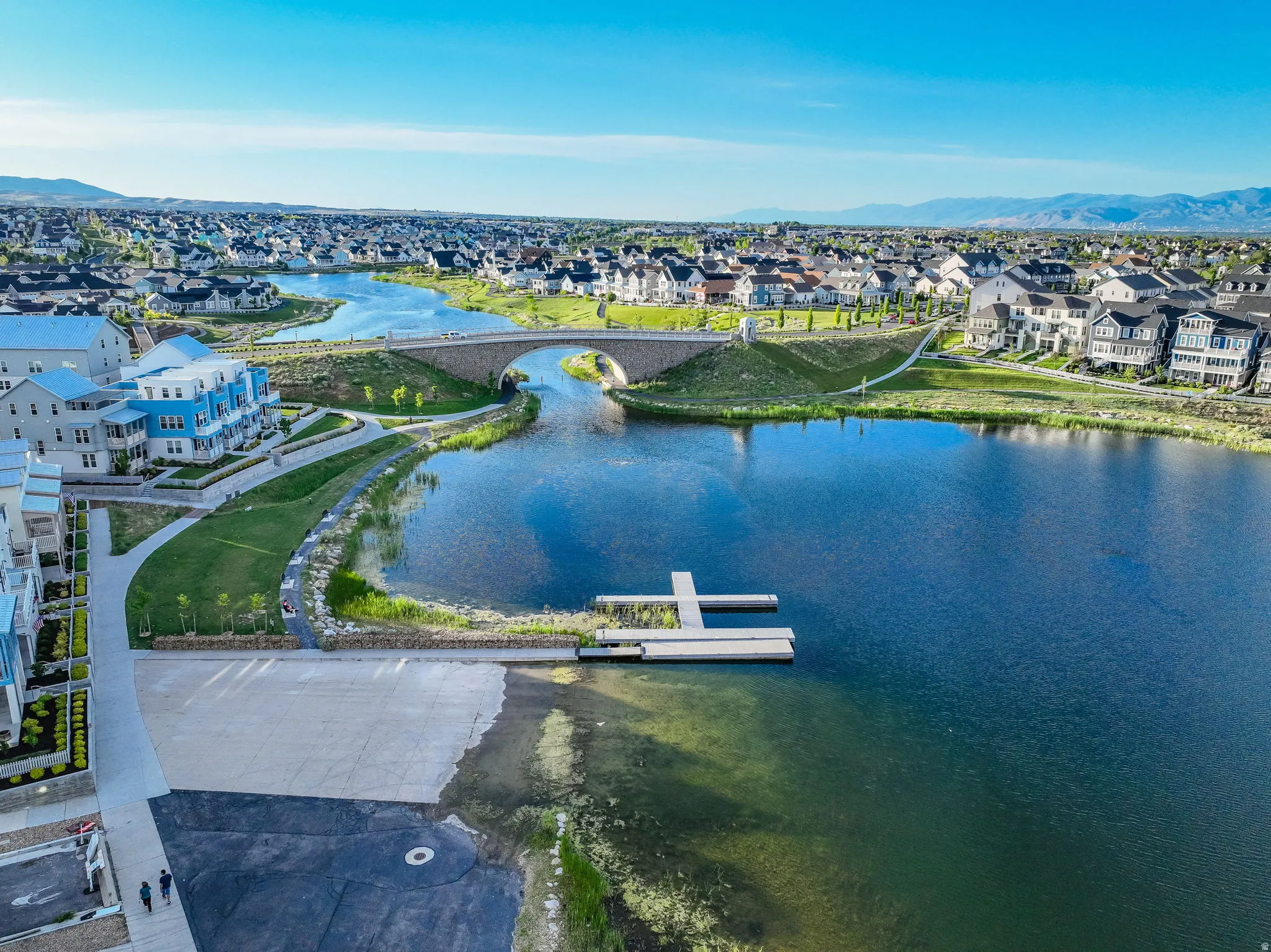 Expansive community lake featuring a floating dock, concrete boat launch, and an arched stone bridge