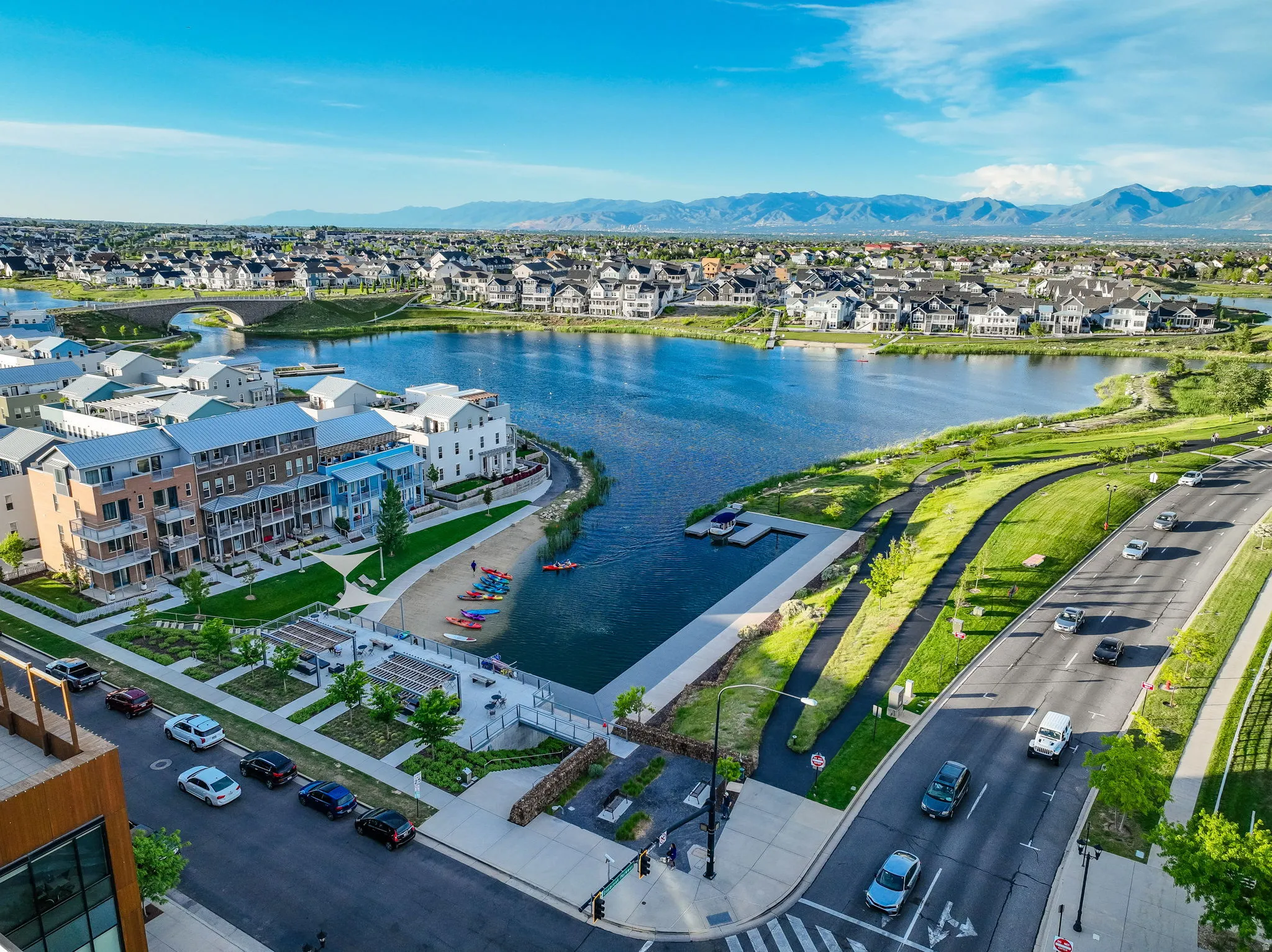 Aerial perspective showcasing a vibrant community with a prominent lake, diverse residential architecture, and surrounding mountainous terrain