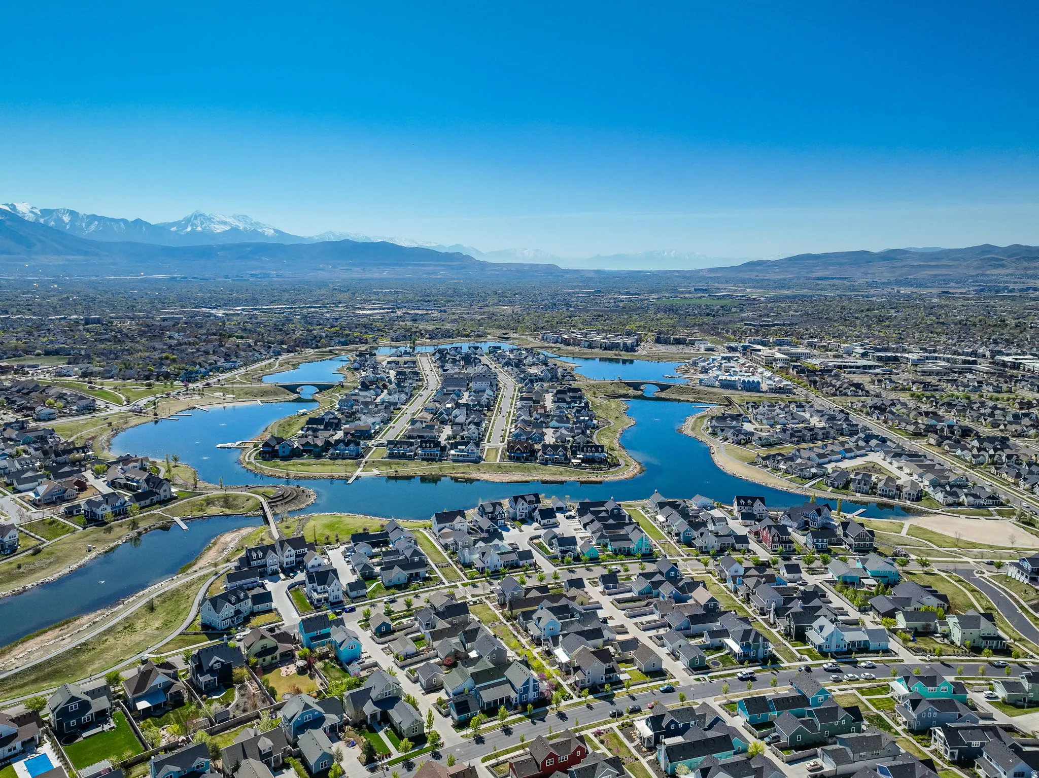 Aerial perspective showcasing a residential community with a winding lake feature, multiple pedestrian bridges, and extensive green spaces