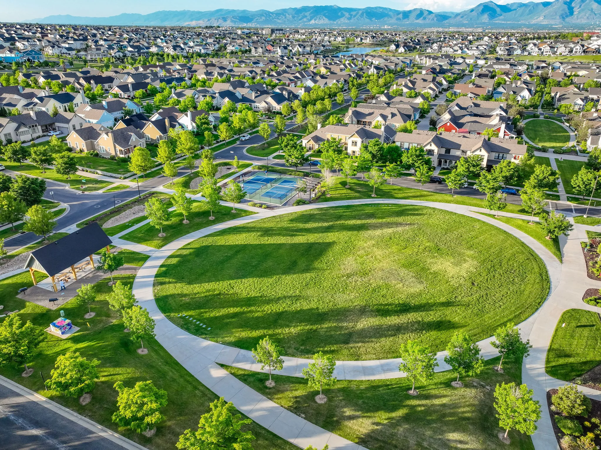 Expansive circular green space surrounded by paved walking paths, mature trees, and a covered pavilion