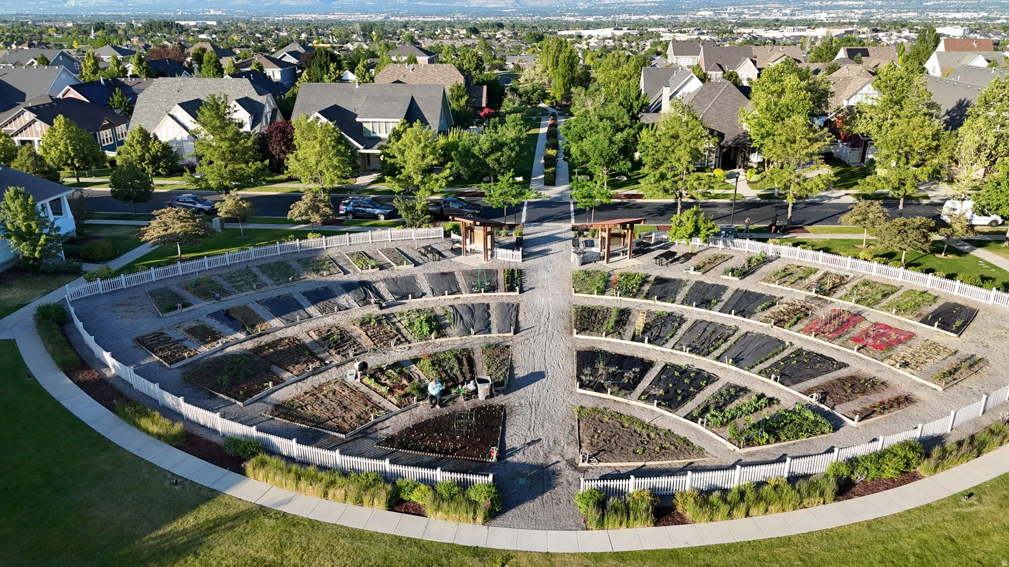 Community garden plots featuring curved retaining walls, gravel pathways, and two central arbors