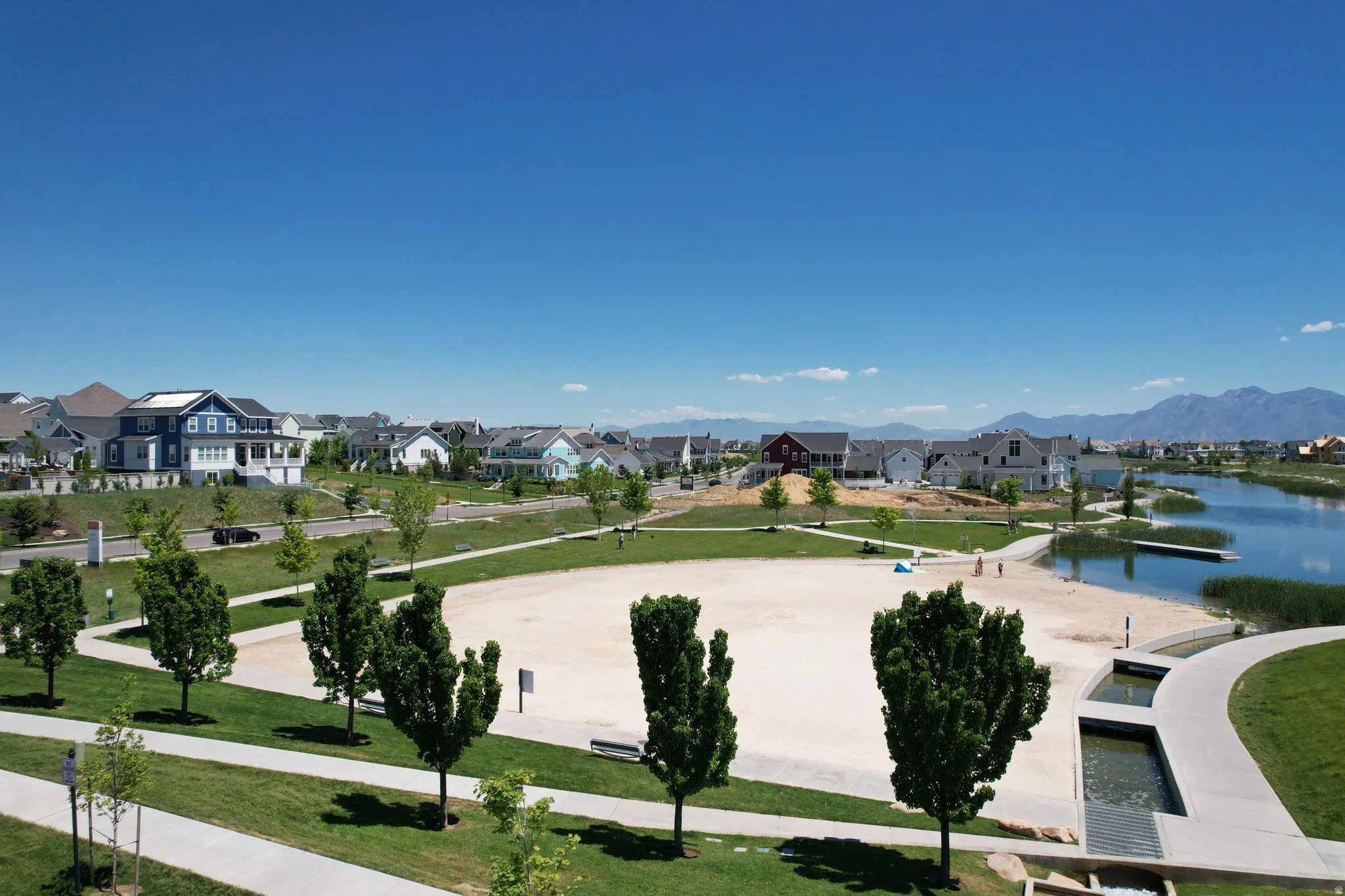 Expansive community green space featuring a sand recreation area, a water feature, and a paved walkway system