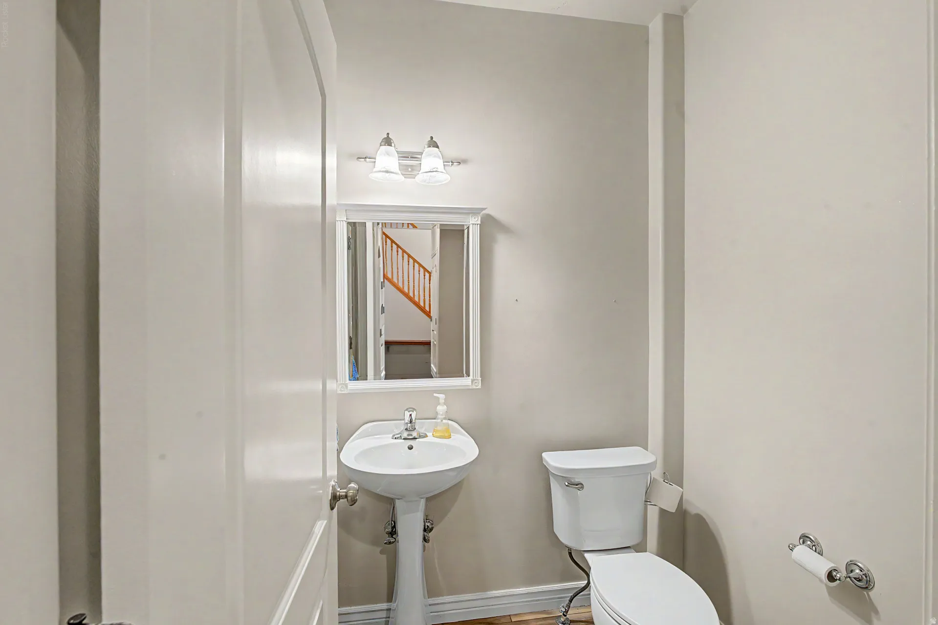 Pedestal sink with chrome fixtures, white framed mirror, and a wall-mounted light fixture with frosted glass shades