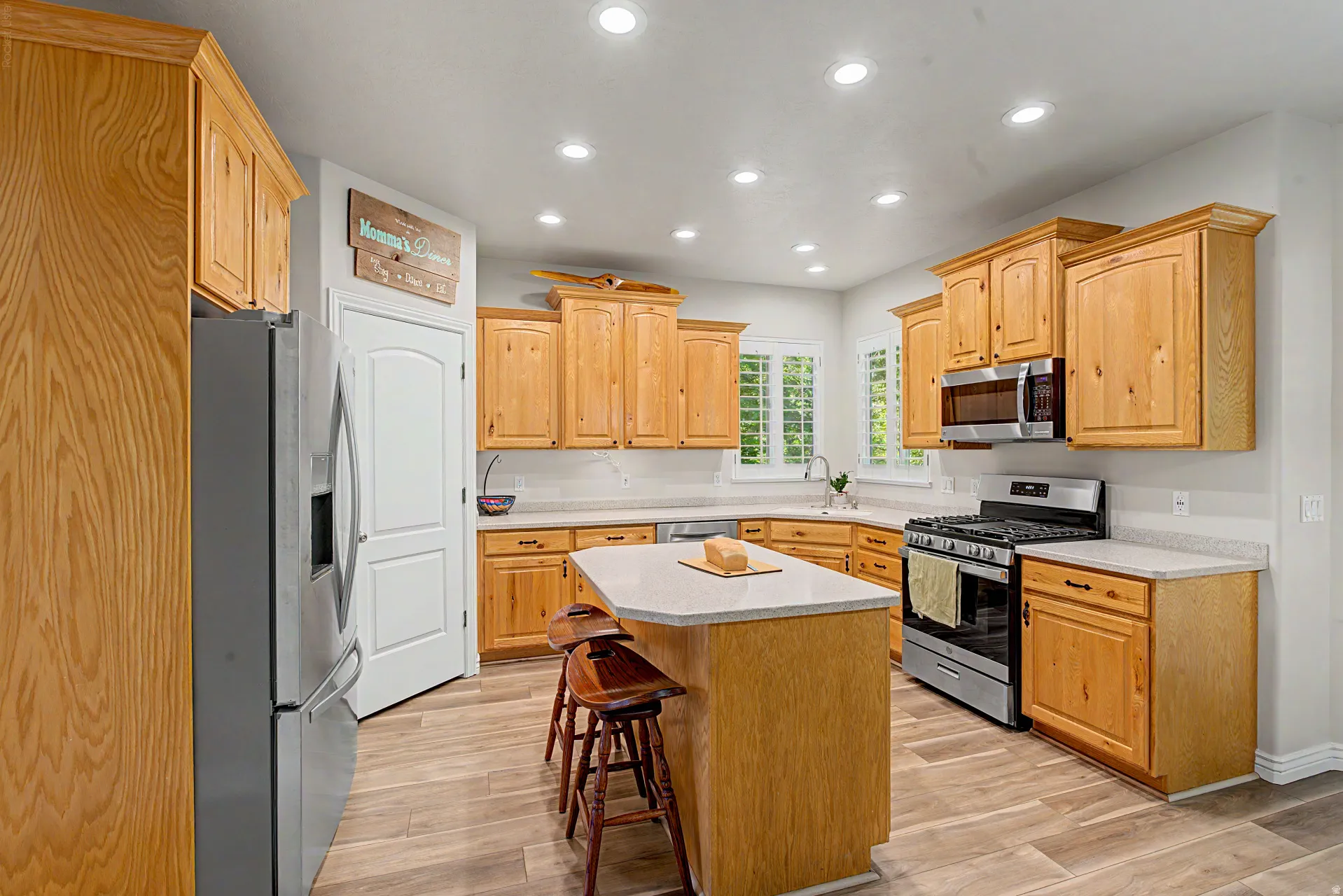 Kitchen featuring wood cabinetry, stainless steel appliances, a center island with seating, recessed lighting, and wood-finish flooring