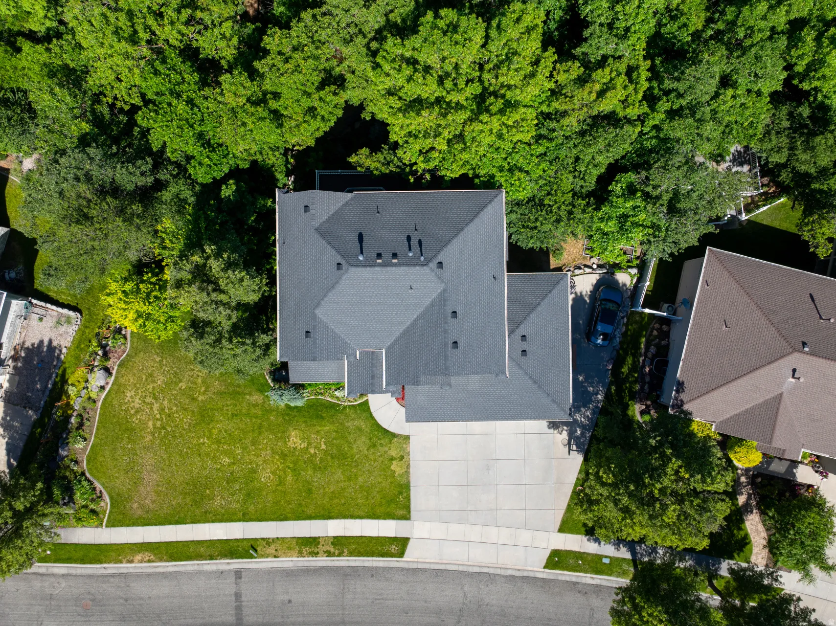 Aerial perspective showcasing a single-family residence with a dark shingle roof, surrounded by mature trees