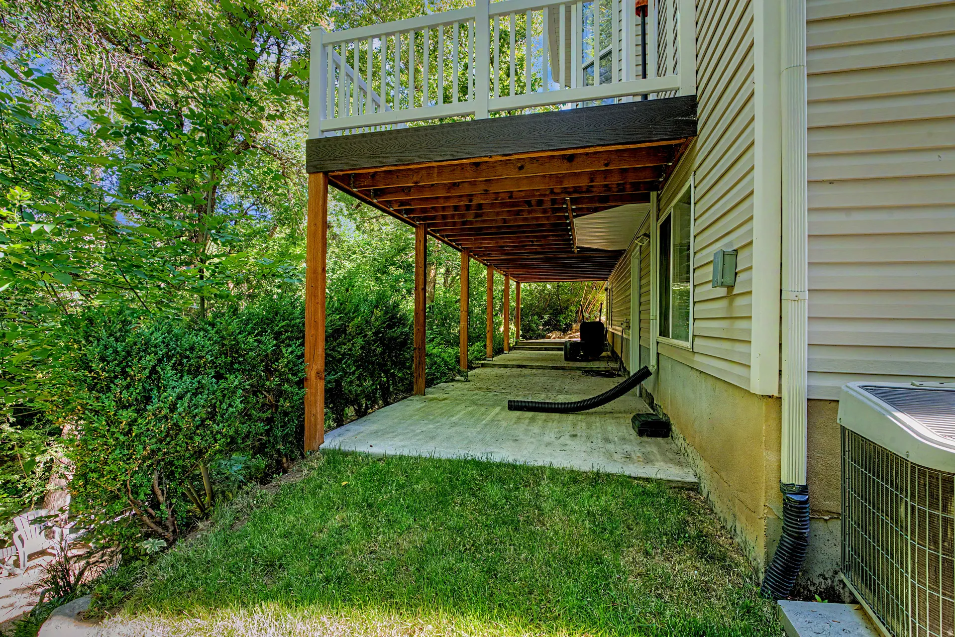 Expansive concrete patio spanning the length of the residence, supported by a wood-framed overhead deck with white railings