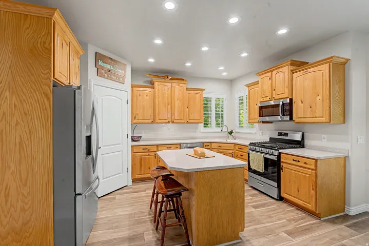 Kitchen featuring wood cabinetry, stainless steel appliances, a center island with seating, recessed lighting, and wood-finish flooring