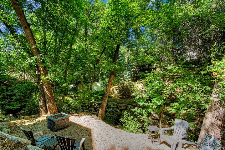 Secluded outdoor area featuring a gravel patio, mature trees, a built-in stone fire pit, and terraced landscaping