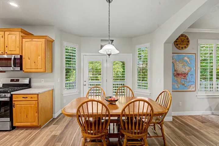 Kitchen dining area featuring wood-finish flooring, light wood cabinetry, stainless steel appliances, and a glass-paned door with side windows