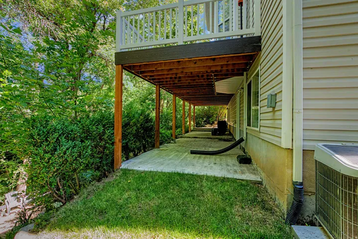 Expansive concrete patio spanning the length of the residence, supported by a wood-framed overhead deck with white railings