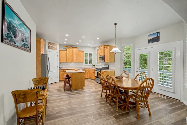 Open-concept kitchen and dining area featuring wood-finish flooring, recessed lighting, and light wood cabinetry