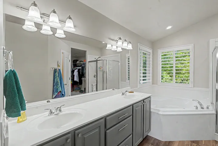 Spacious bathroom featuring a dual vanity with grey cabinetry, a large soaking tub, and a separate glass-enclosed shower
