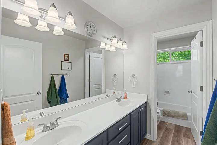 Bathroom featuring a dual vanity with a white countertop and dark cabinetry, wood-finish flooring, a full mirror, and a bathtub with an overhead window