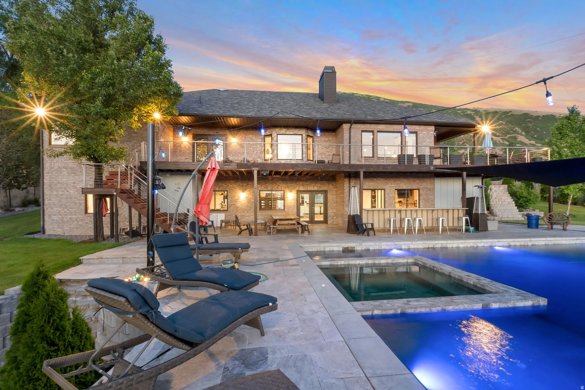Spacious outdoor living area featuring a large swimming pool with an integrated spa, extensive stone patio, and an outdoor bar