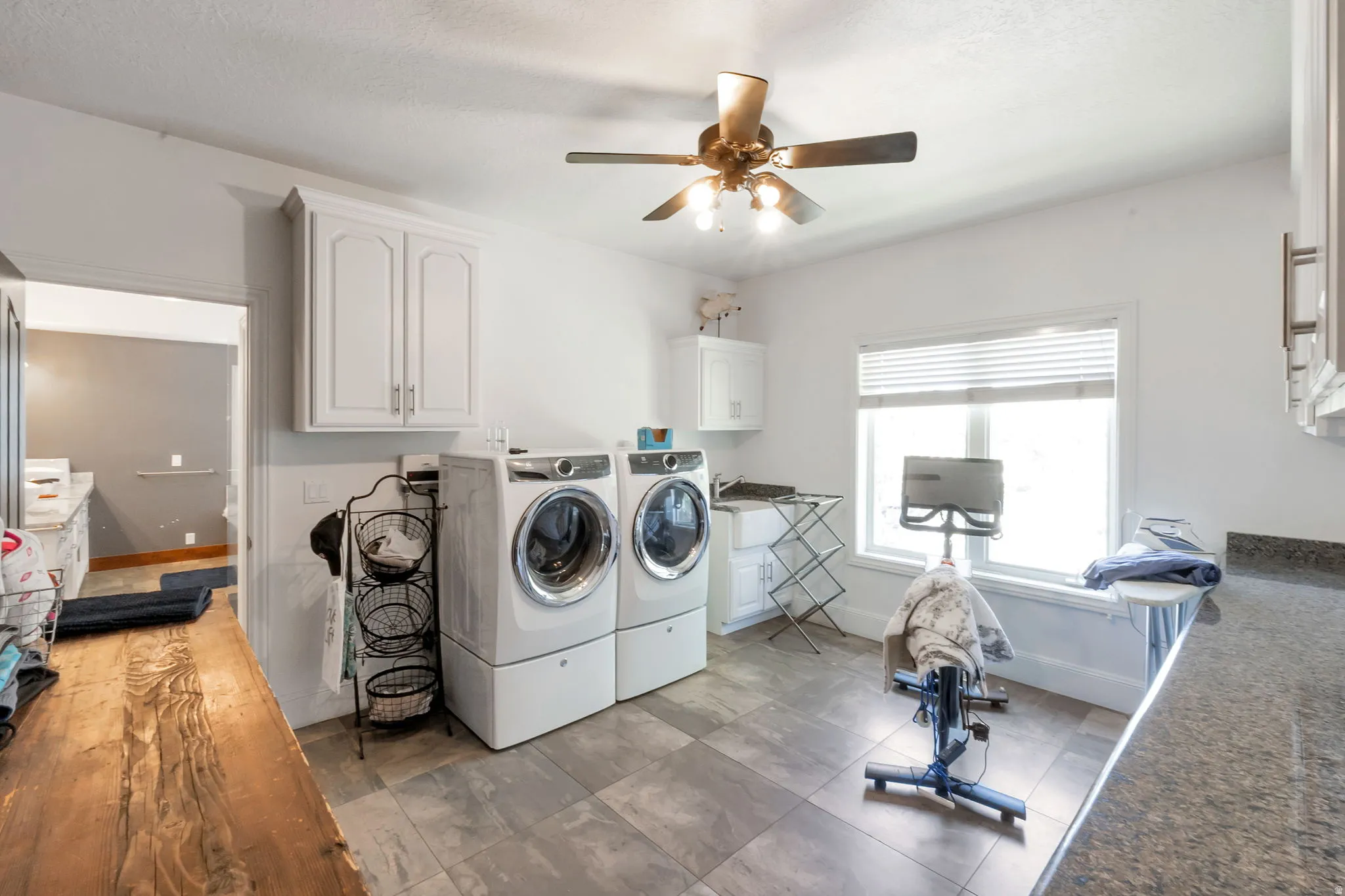 Spacious utility room featuring tile flooring, white cabinetry, a built-in sink, and a countertop with a stone-finish surface
