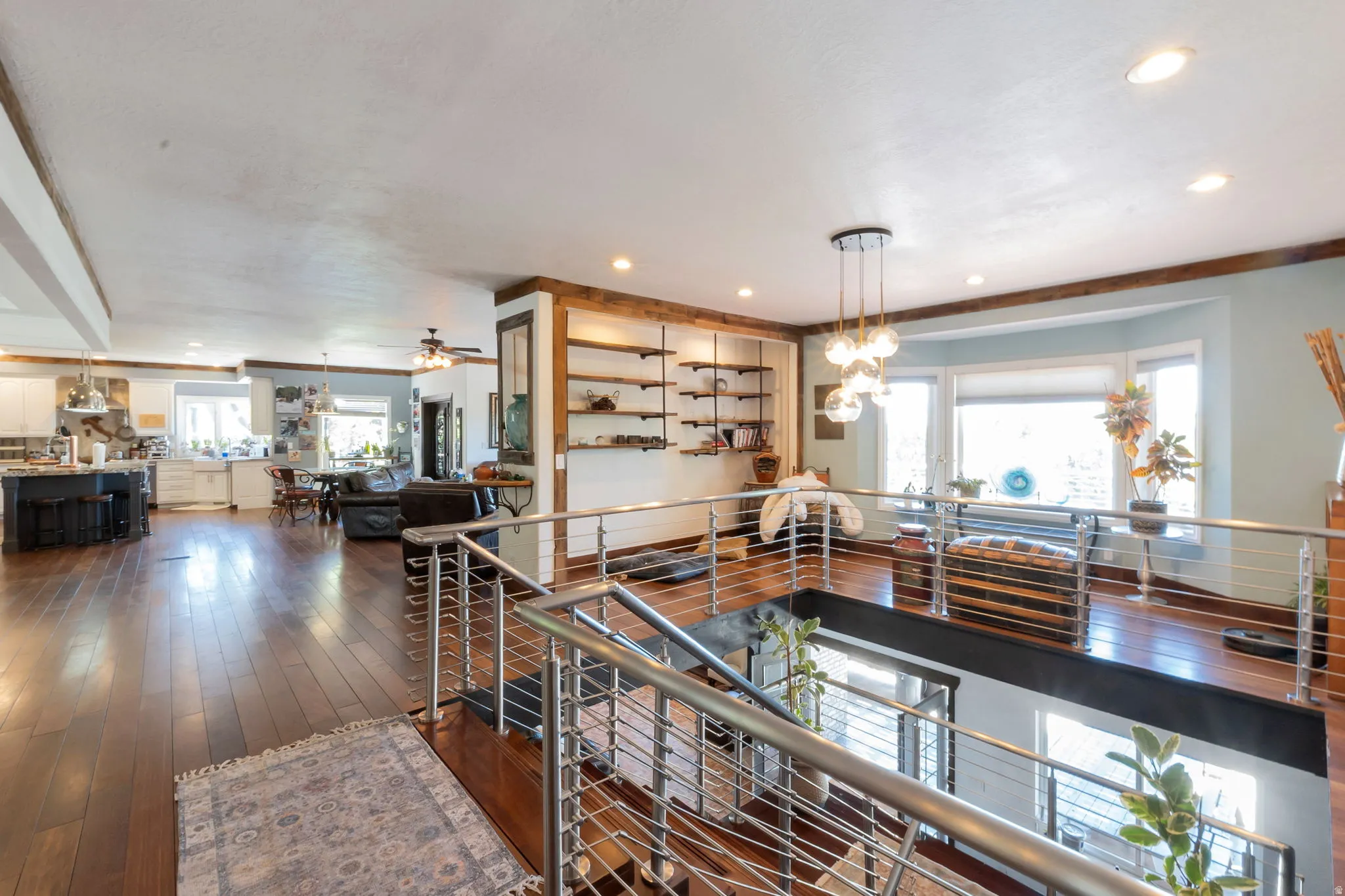 Open-concept interior featuring wood-finish flooring, a modern cable railing system, a contemporary pendant light fixture, built-in shelving, and a bay window
