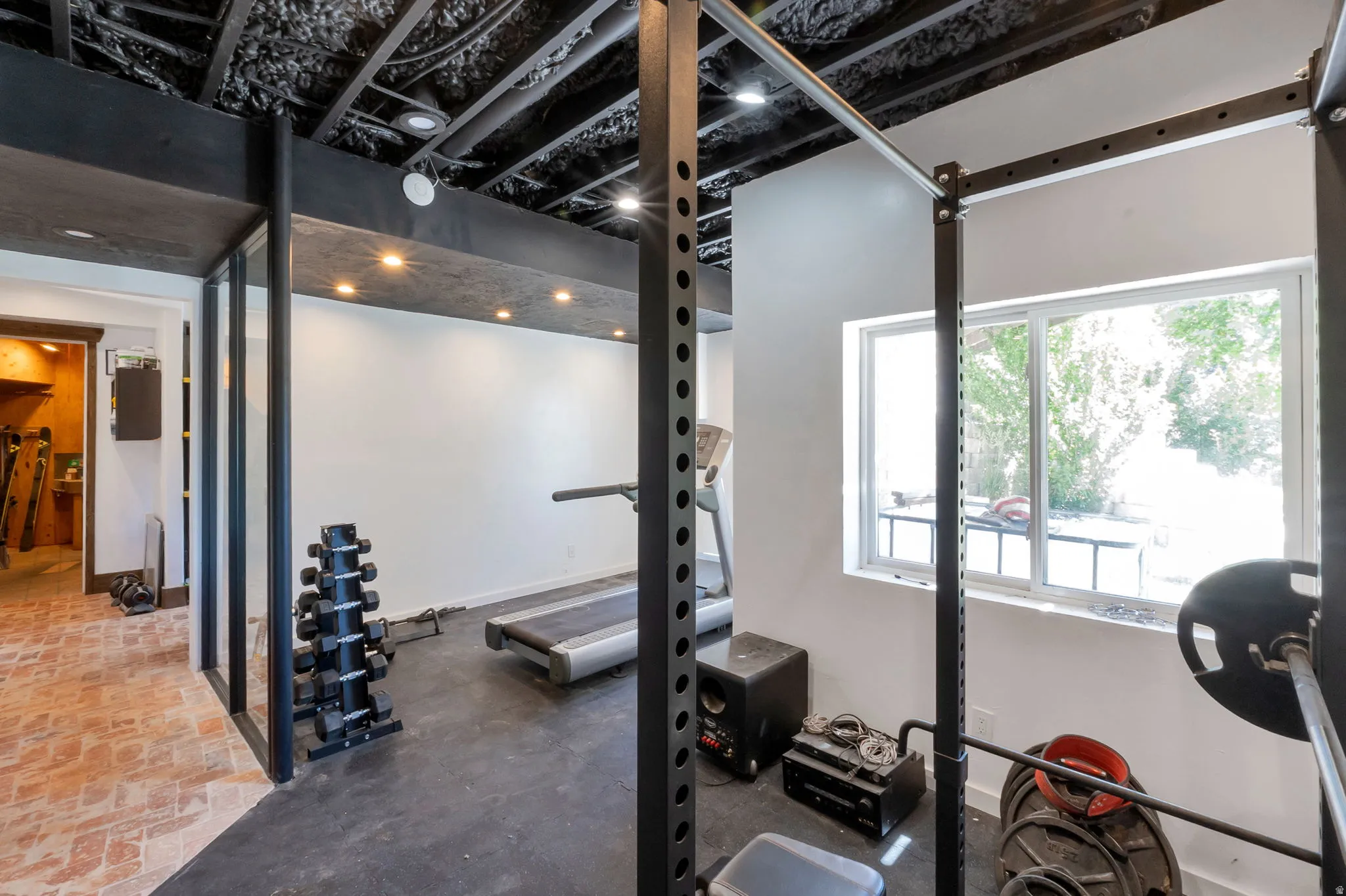 Dedicated exercise space featuring a black rubber floor, white walls, and an exposed black ceiling with recessed lighting