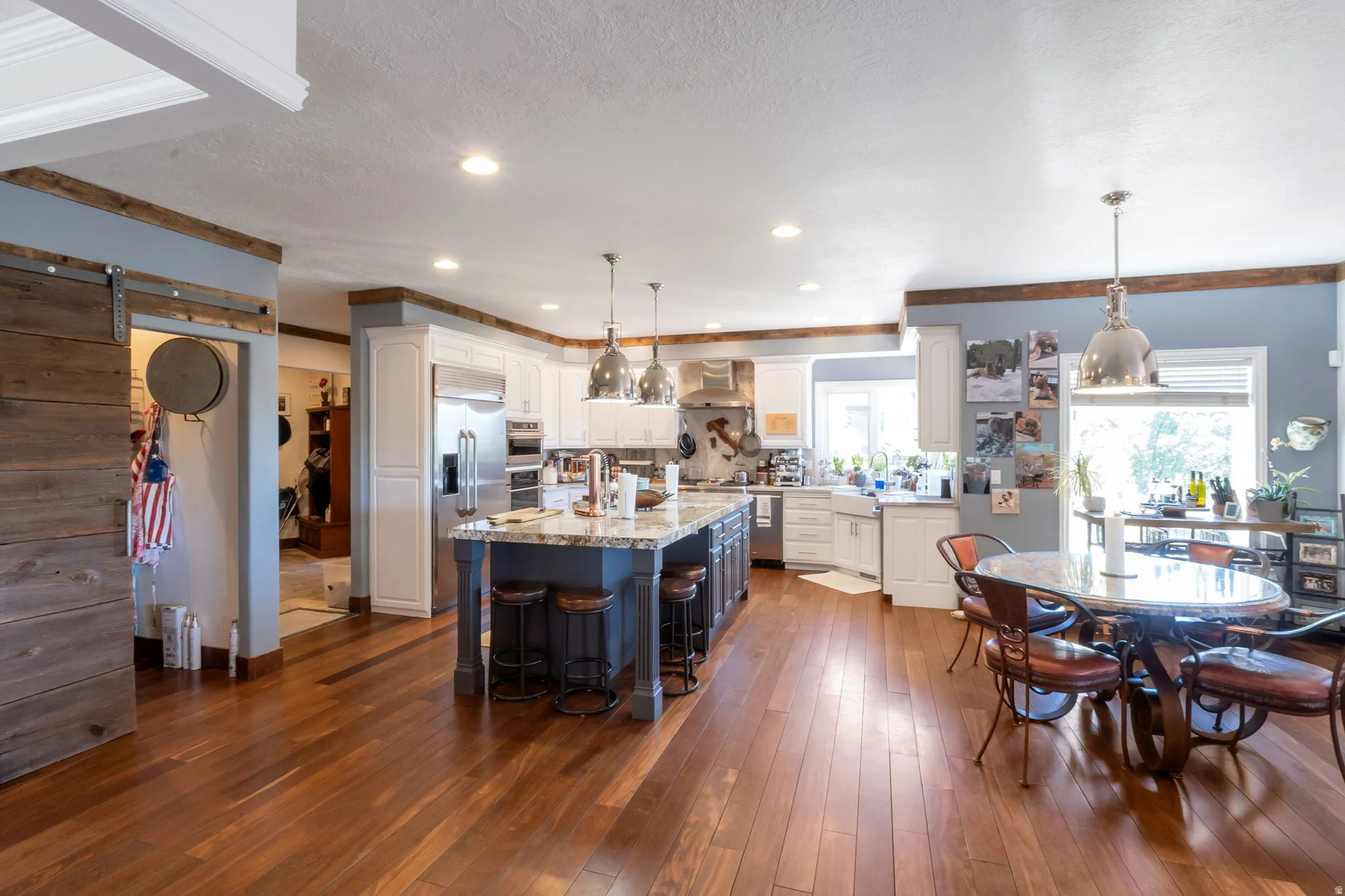 Open-concept kitchen and dining area featuring rich wood-finish flooring, a substantial kitchen island with a stone countertop, white cabinetry, and Stainlesss Steel GE Monogram appliances.