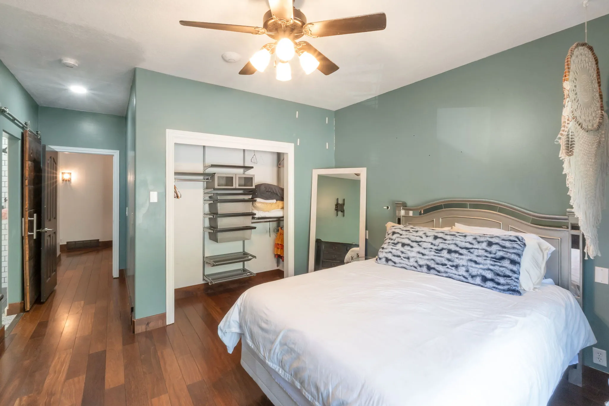 Room featuring wood-finish flooring, a ceiling fan with integrated lighting, and a built-in closet with modular shelving