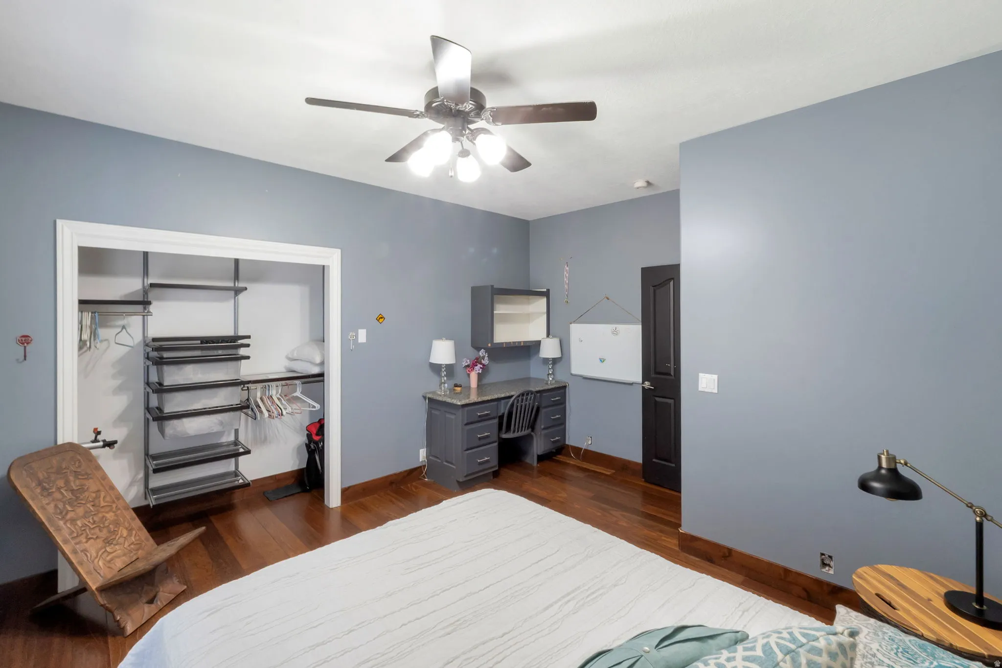 Bedroom featuring wood-finish flooring, a ceiling fan with integrated lighting, and a built-in desk with cabinetry