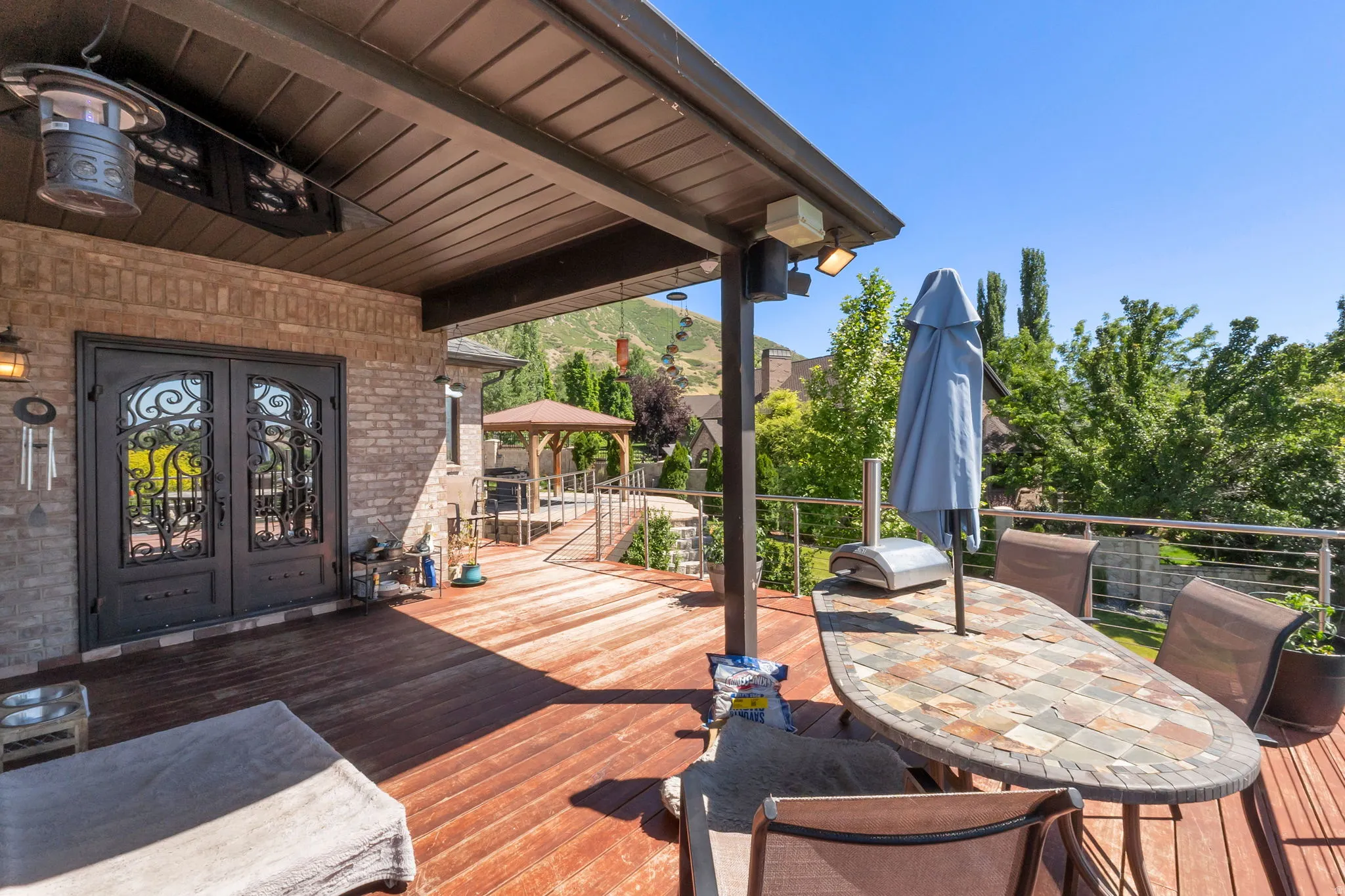 Spacious outdoor deck featuring rich wood-finish flooring, a covered patio area, and a metal railing system, outside entertain with TV.