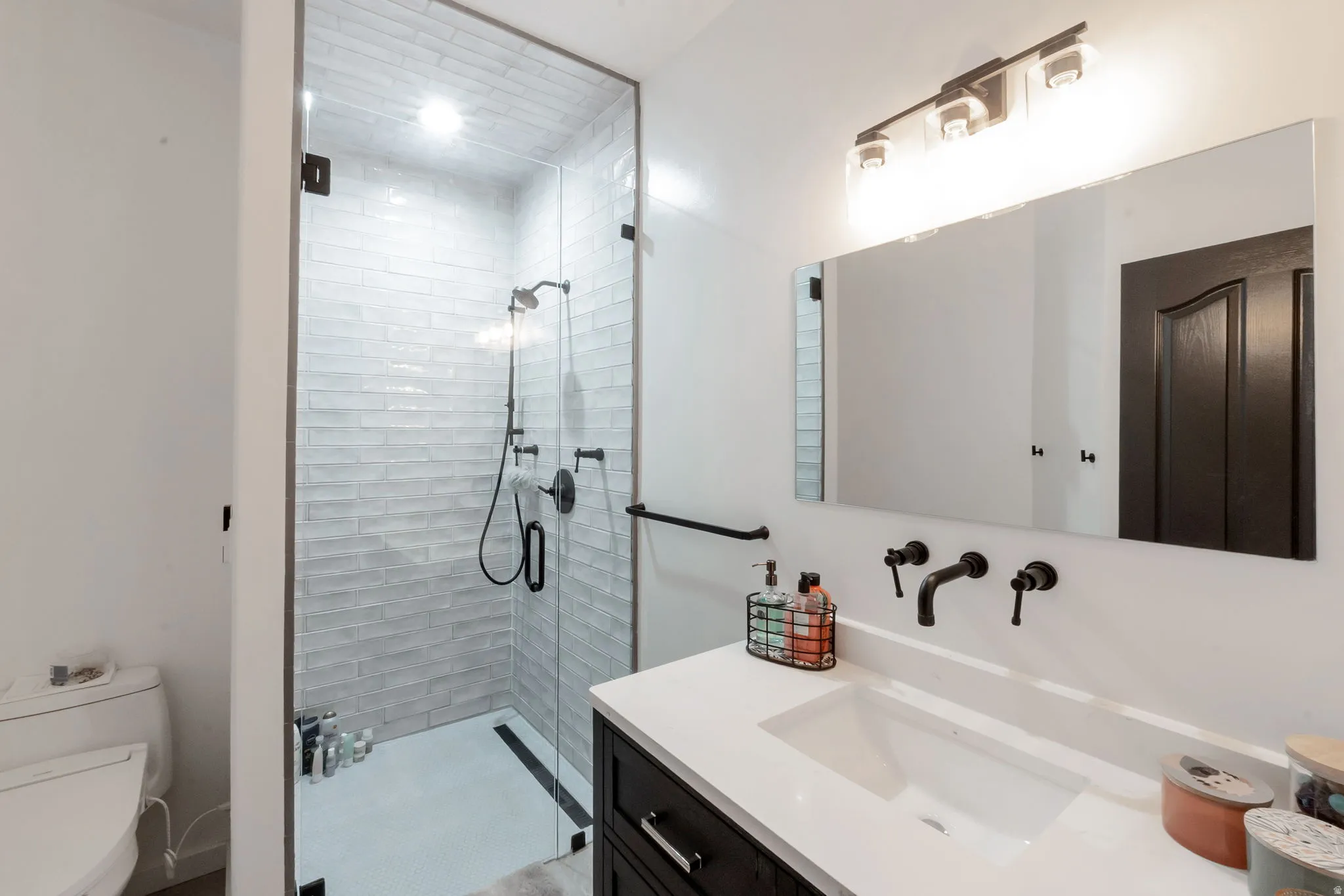 Modern bathroom featuring a glass-enclosed shower with subway tile surround and black fixtures