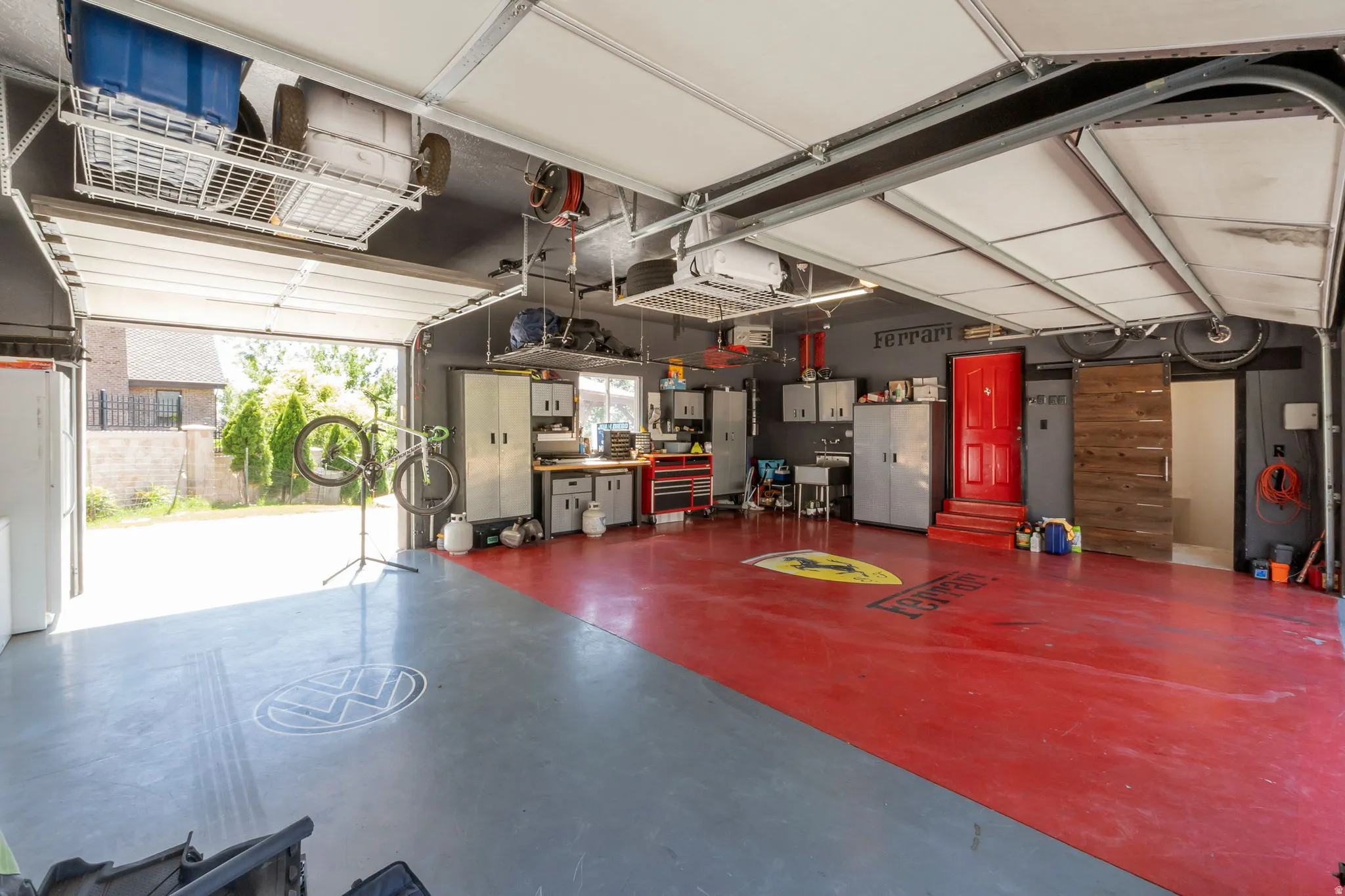 Spacious heated garage featuring a red and gray epoxy floor, overhead storage racks, built-in cabinetry, a utility sink, and a sliding wood-finish barn door