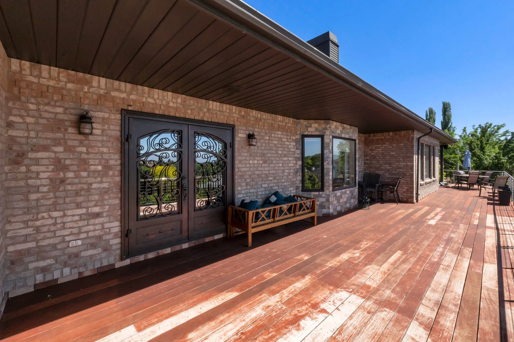 Expansive wood-plank deck featuring a brick exterior, decorative iron double doors,