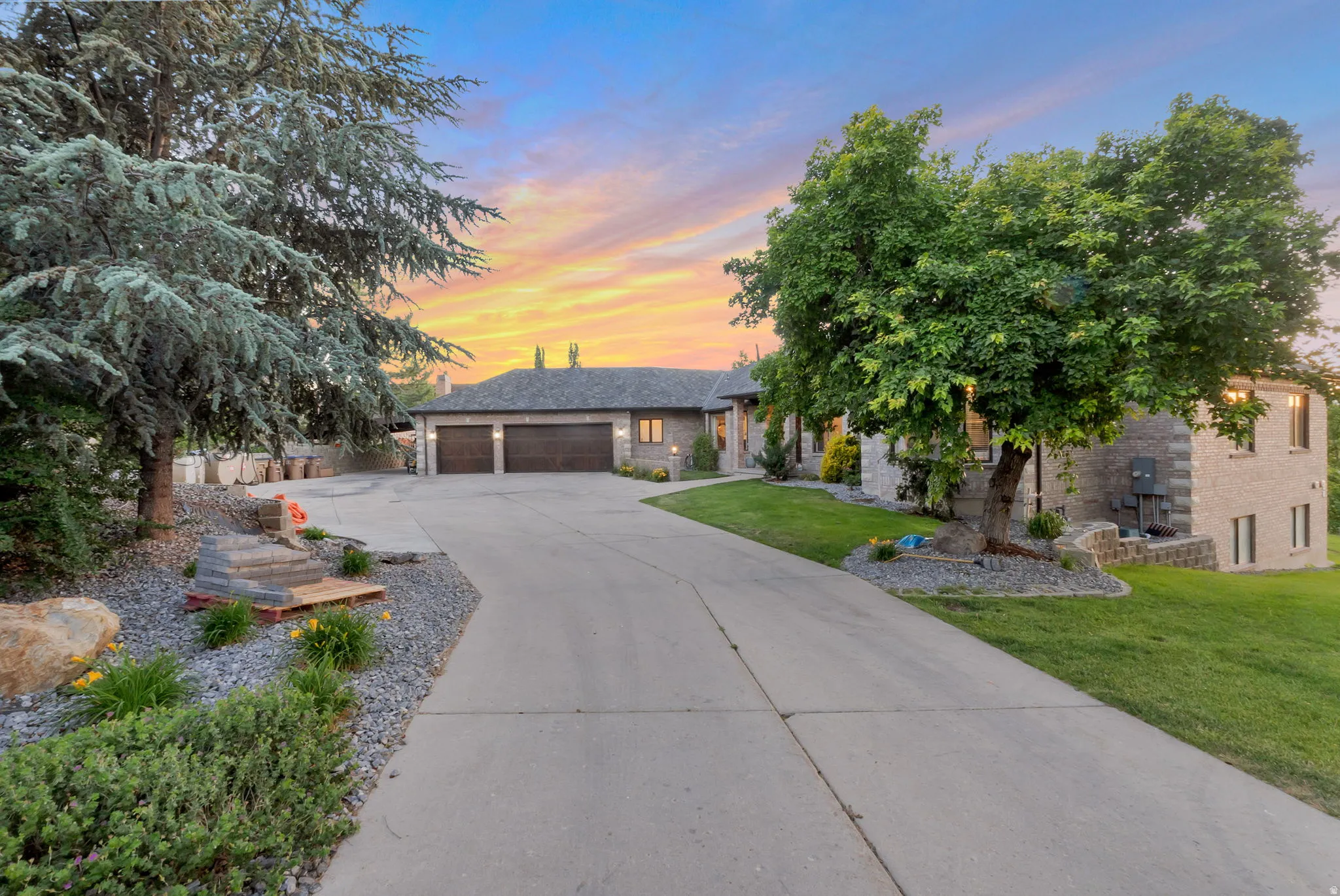 Stone-clad residence featuring a concrete driveway, three-car garage , and extensive rock landscaping