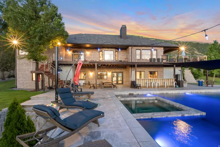 Spacious outdoor living area featuring a large swimming pool with an integrated spa, extensive stone patio, and an outdoor bar