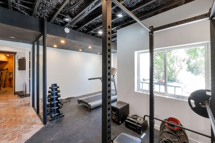 Dedicated exercise space featuring a black rubber floor, white walls, and an exposed black ceiling with recessed lighting