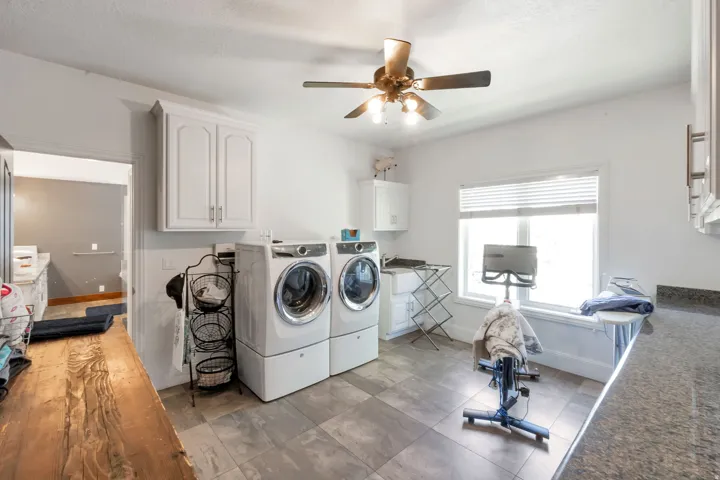 Spacious utility room featuring tile flooring, white cabinetry, a built-in sink, and a countertop with a stone-finish surface