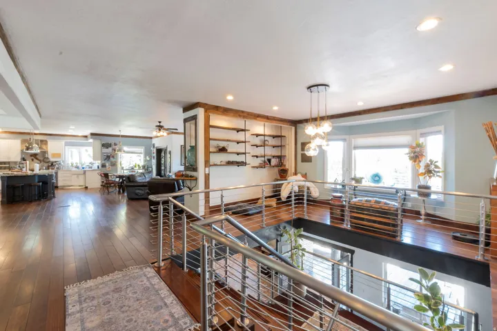 Open-concept interior featuring wood-finish flooring, a modern cable railing system, a contemporary pendant light fixture, built-in shelving, and a bay window