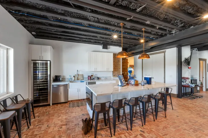 Kitchen space featuring an exposed ceiling with dark beams, brick-patterned flooring, white cabinetry, a large center island with a light-colored countertop, and a built-in wine refrigerator