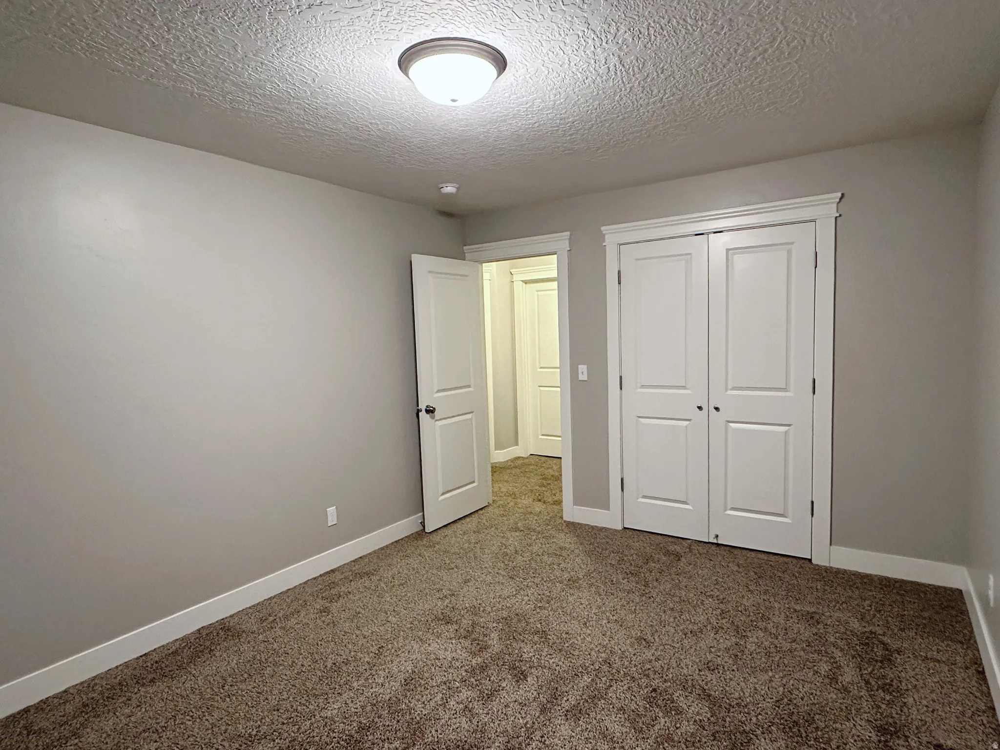 Carpeted room featuring a white bi-fold closet, a white interior door with black hardware, neutral wall paint, and a semi-flush mount ceiling light