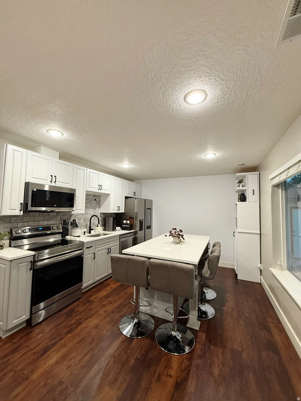 Kitchen featuring a central island with countertop seating, wood-finish flooring, stainless steel appliances, white cabinetry, and recessed lighting
